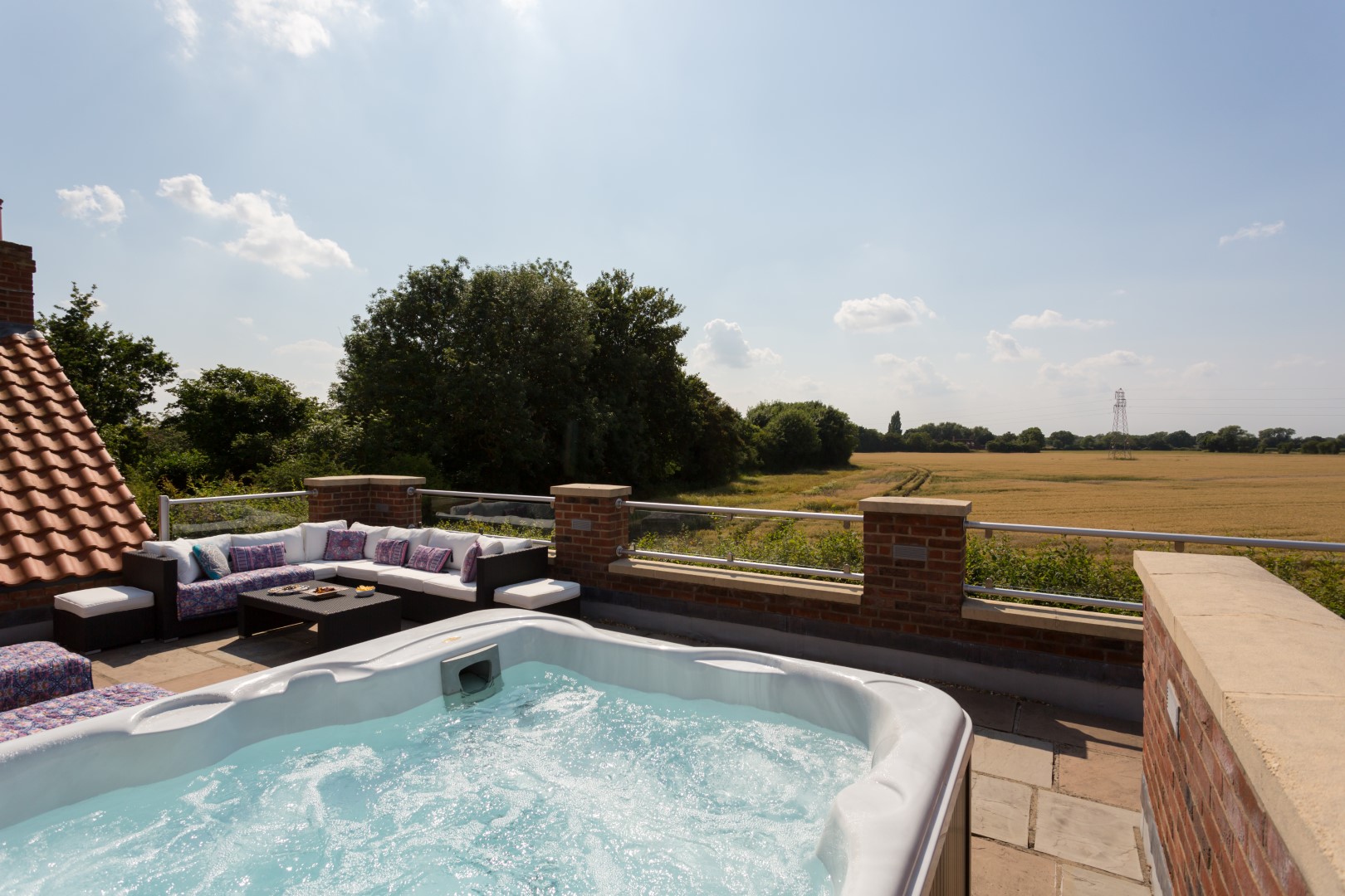 Experience the ultimate UK Hot Tub Holidays on a rooftop patio, featuring a hot tub, outdoor seating, and a captivating countryside view under a partly cloudy sky.