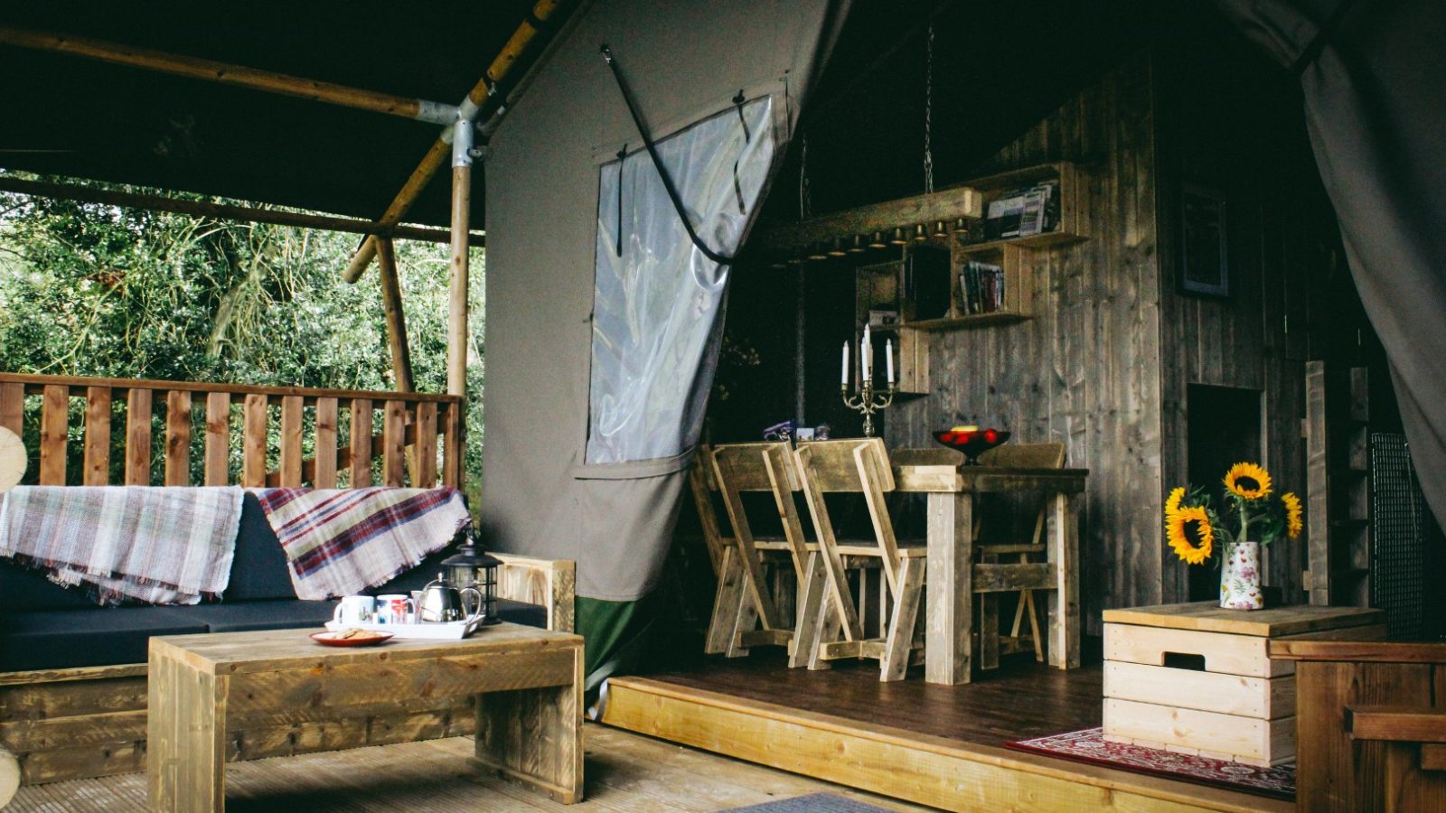 The rustic cabin interior resembles a Stellar Safari Lodge, with wooden furniture, a cozy couch adorned with blankets, a charming coffee table set, and vibrant sunflowers placed on a vintage box.