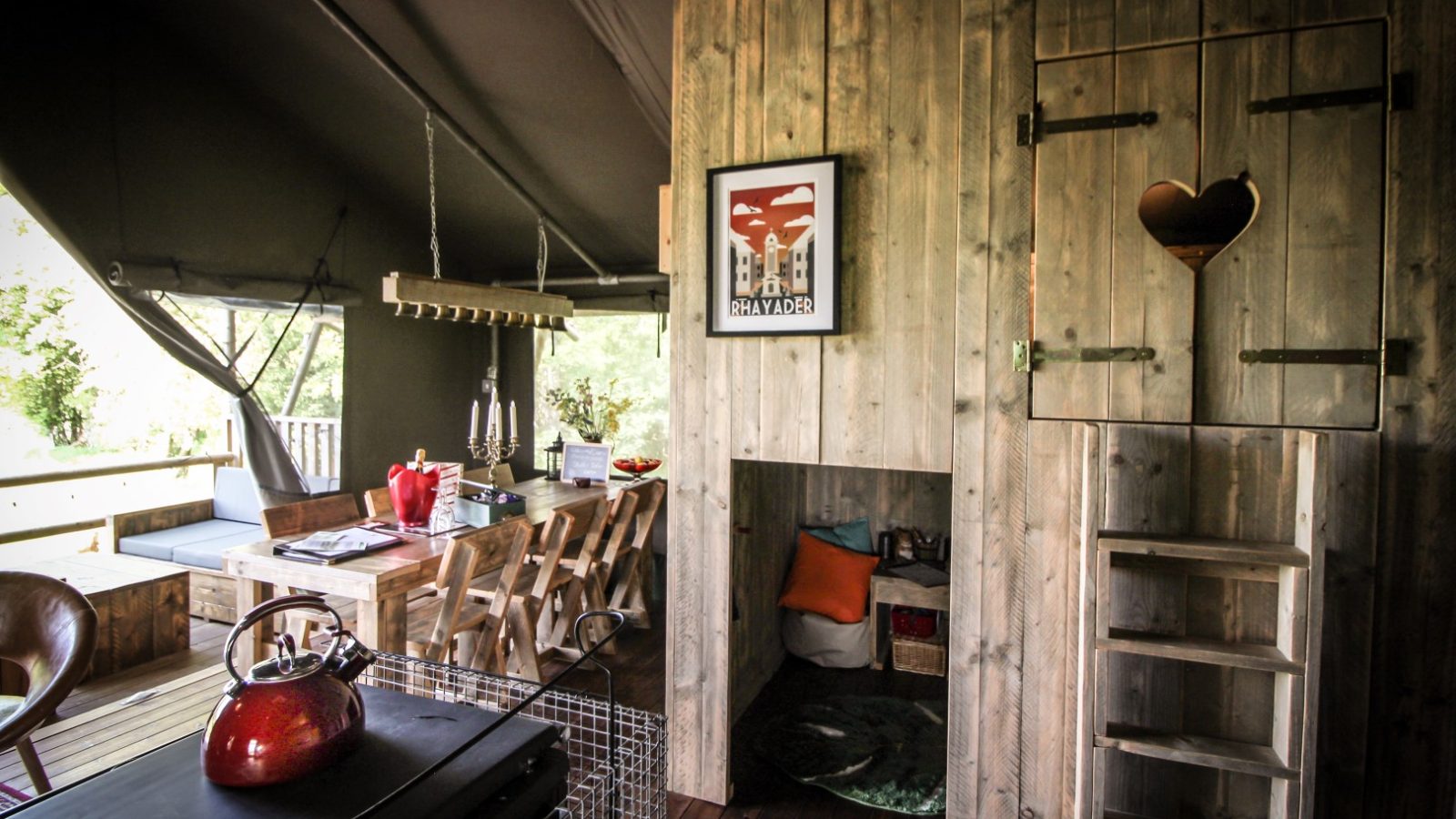 Cozy wooden cabin interior reminiscent of a Stellar Safari Lodge, featuring a dining table, red kettle on the stove, wall art, and a loft access ladder.