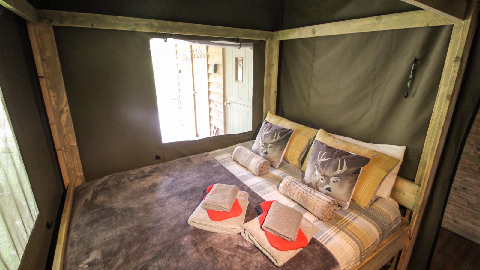 Cozy wooden bed with plaid bedding, two deer-themed throw pillows, and neatly folded towels on a soft brown blanket, capturing the essence of the Stellar Safari Lodge's rustic charm.