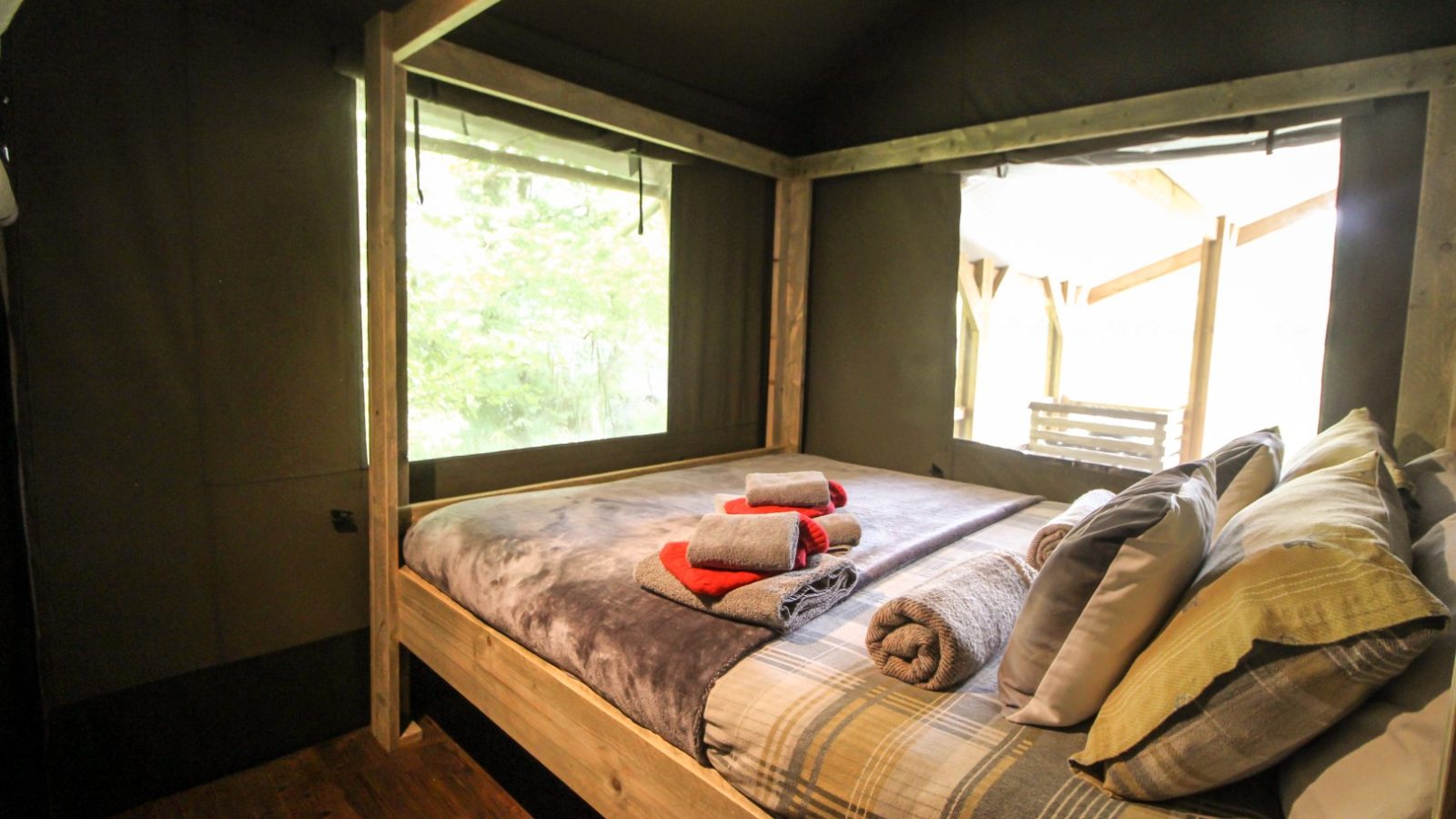 A cozy Stellar Safari Lodge bedroom with a large bed, stacked pillows, and folded towels. Light streams in through expansive windows.