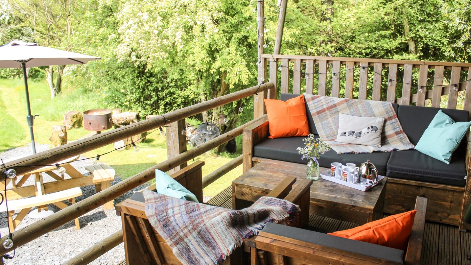 Experience the cozy outdoor seating area at Stellar Safari Lodge, complete with wooden furniture, colorful cushions, and a warm blanket. Nearby awaits a picnic table surrounded by the lush green garden, perfect for relaxation and immersing yourself in nature's tranquility.