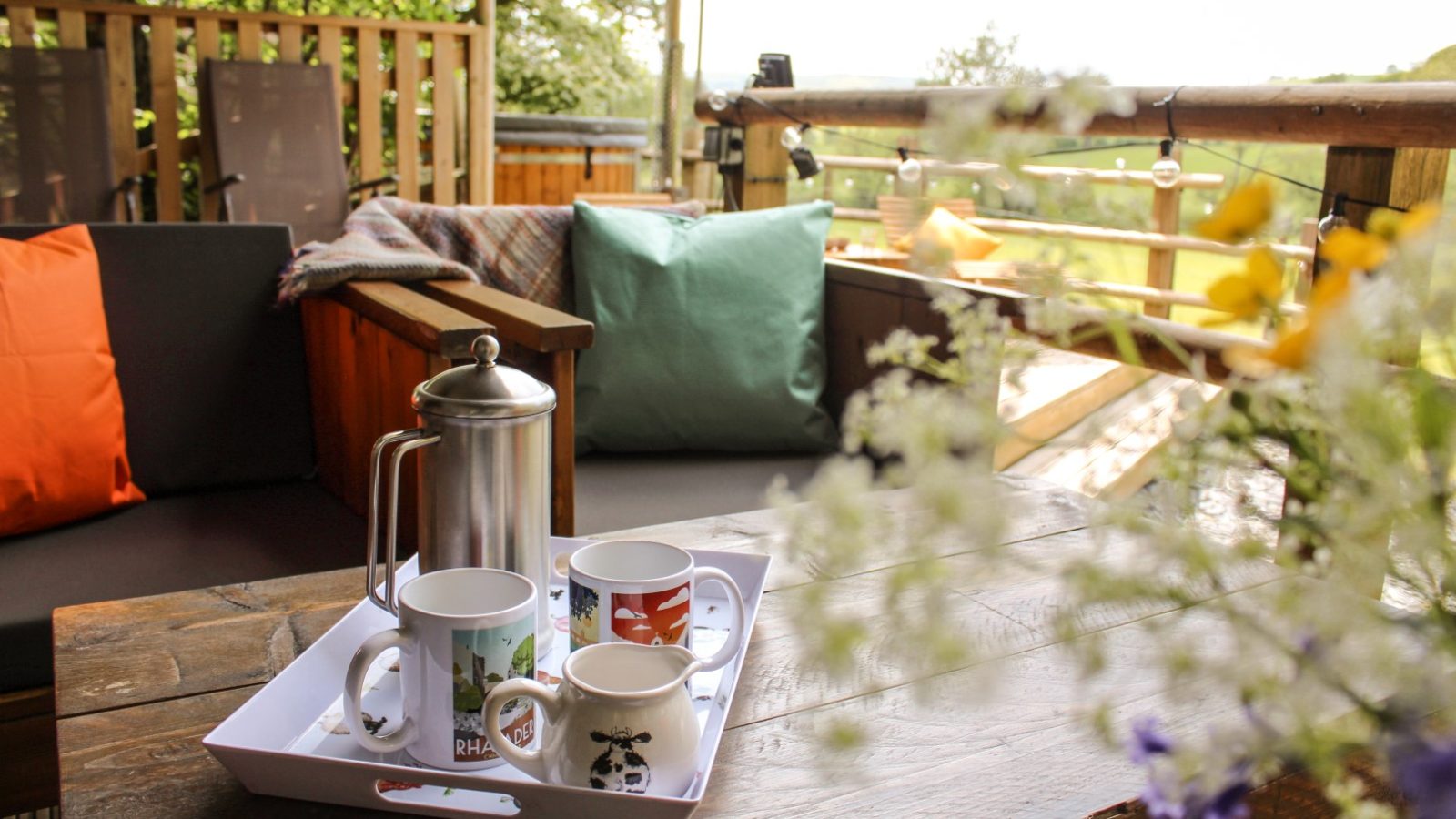 A patio table at Stellar Safari Lodge features a tray with a French press and four mugs, inviting you for a tranquil coffee break. Cushioned chairs offer comfort as you soak in the lush greenery that surrounds this serene escape.