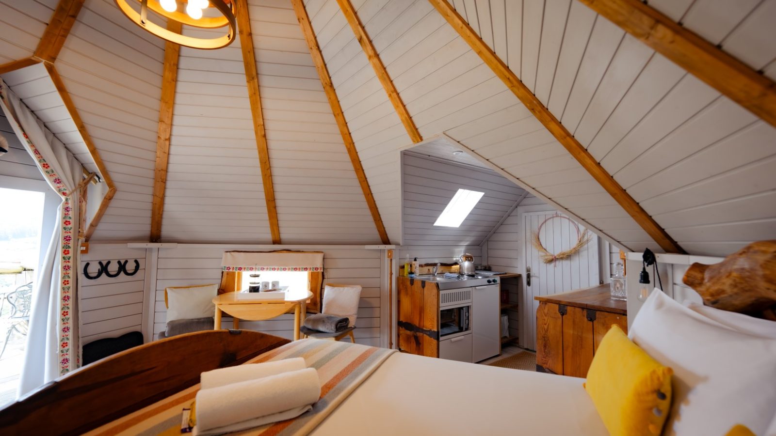 The cosy cabin interior feels like a fantasy retreat, with its bed, small kitchen, dining area, and wooden beams. A skylight brightens the space. Dragons Gate Glamping cabins in herefordshire