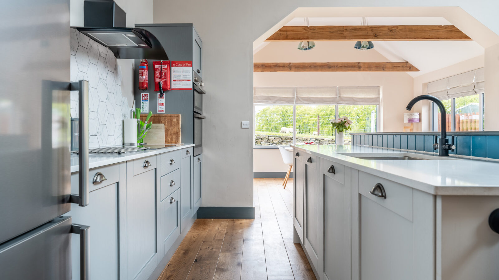 This bright kitchen in Stabl Nantcoy features light wood flooring, white cabinets, stainless steel appliances, and large windows that flood the space with natural light.