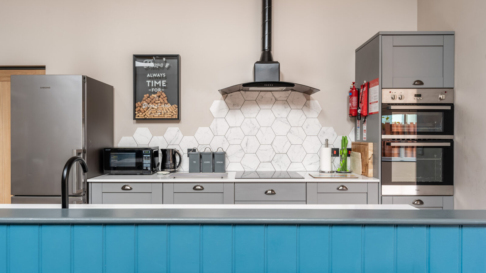 The modern kitchen features a blue Stabl Nantcoy island, hexagonal tile backsplash, sleek gray cabinets, top-tier appliances, and a stylish wall clock.