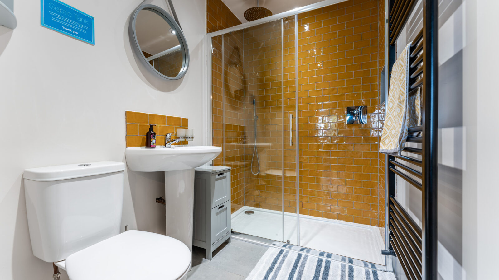 In the modern bathroom, a white toilet and sink complement the orange-tiled shower area, reminiscent of a cozy retreat at Stabl Nantcoy. A round mirror reflects style, while a striped rug adds warmth.