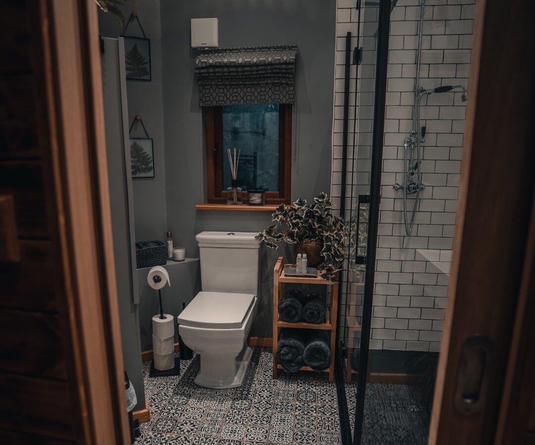 A small bathroom with a patterned tile floor, a toilet, and a glass shower enclosure offers the cozy charm of a woodland retreat.