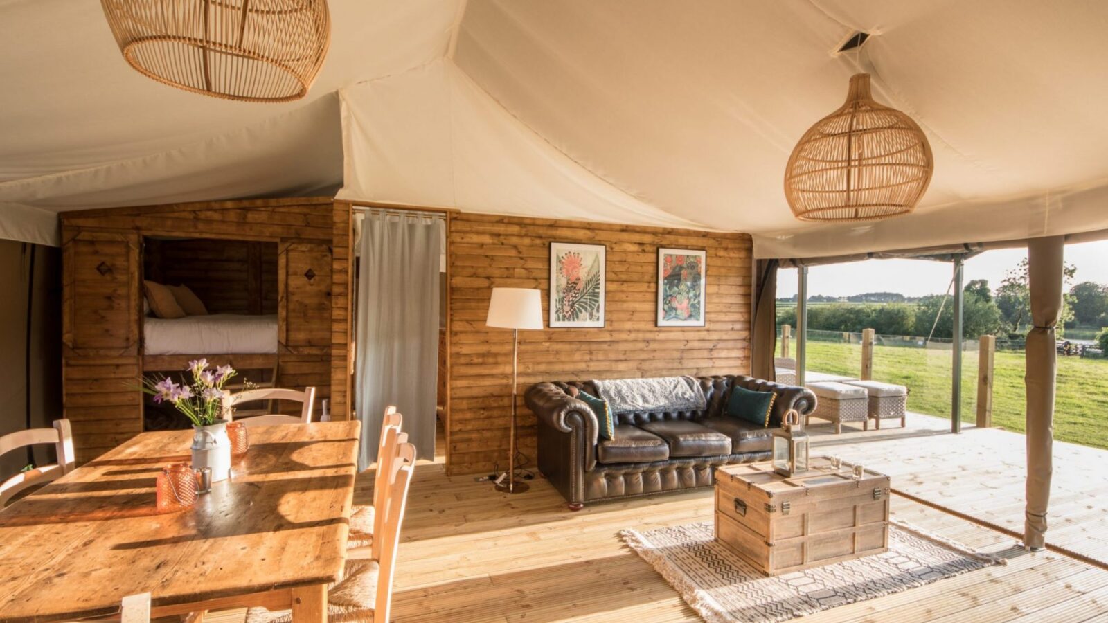 Nest Glamping offers a cozy tent interior featuring wooden furniture, a leather sofa, and decorative lighting that beautifully overlooks a green field.