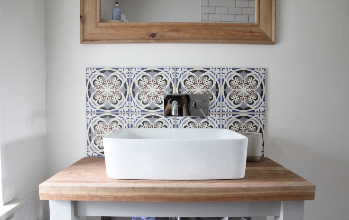 The Pheasant Cottage bathroom vanity features a white rectangular sink, wooden countertop, decorative tile backsplash, and a wall-mounted faucet, perfectly combining rustic charm with modern elegance.