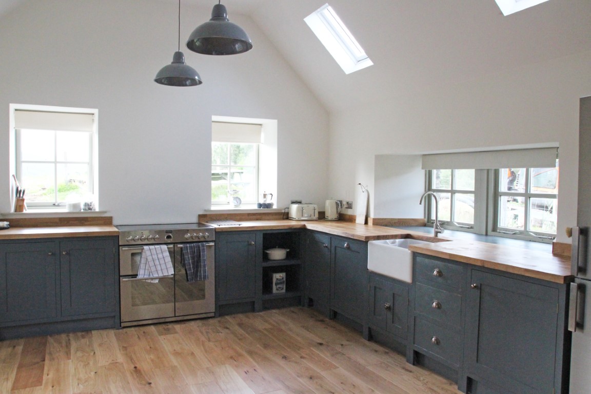 The modern Pheasant Cottage kitchen features gray cabinets, wooden countertops, a farmhouse sink, and stainless steel appliances, all beautifully illuminated by skylights.