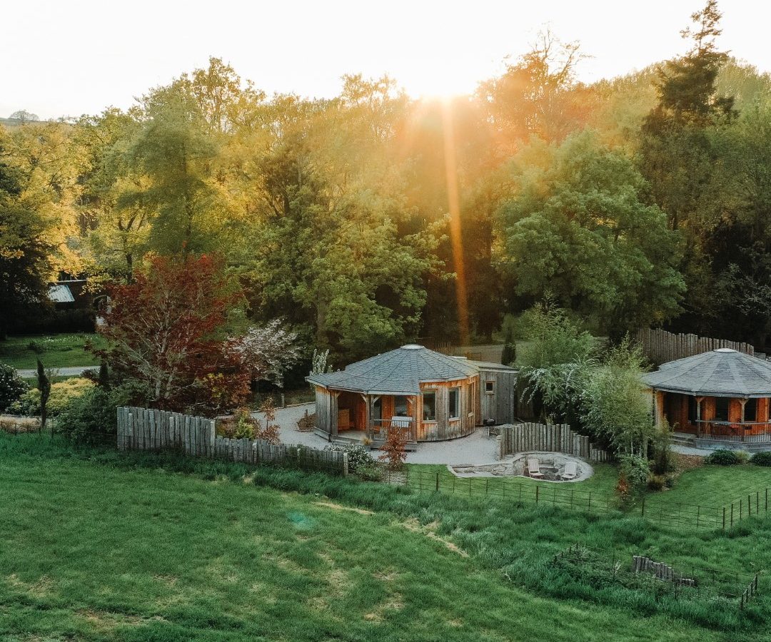 A serene retreat, featuring wooden gazebos surrounded by lush greenery and trees, offers a peaceful escape at sunset.