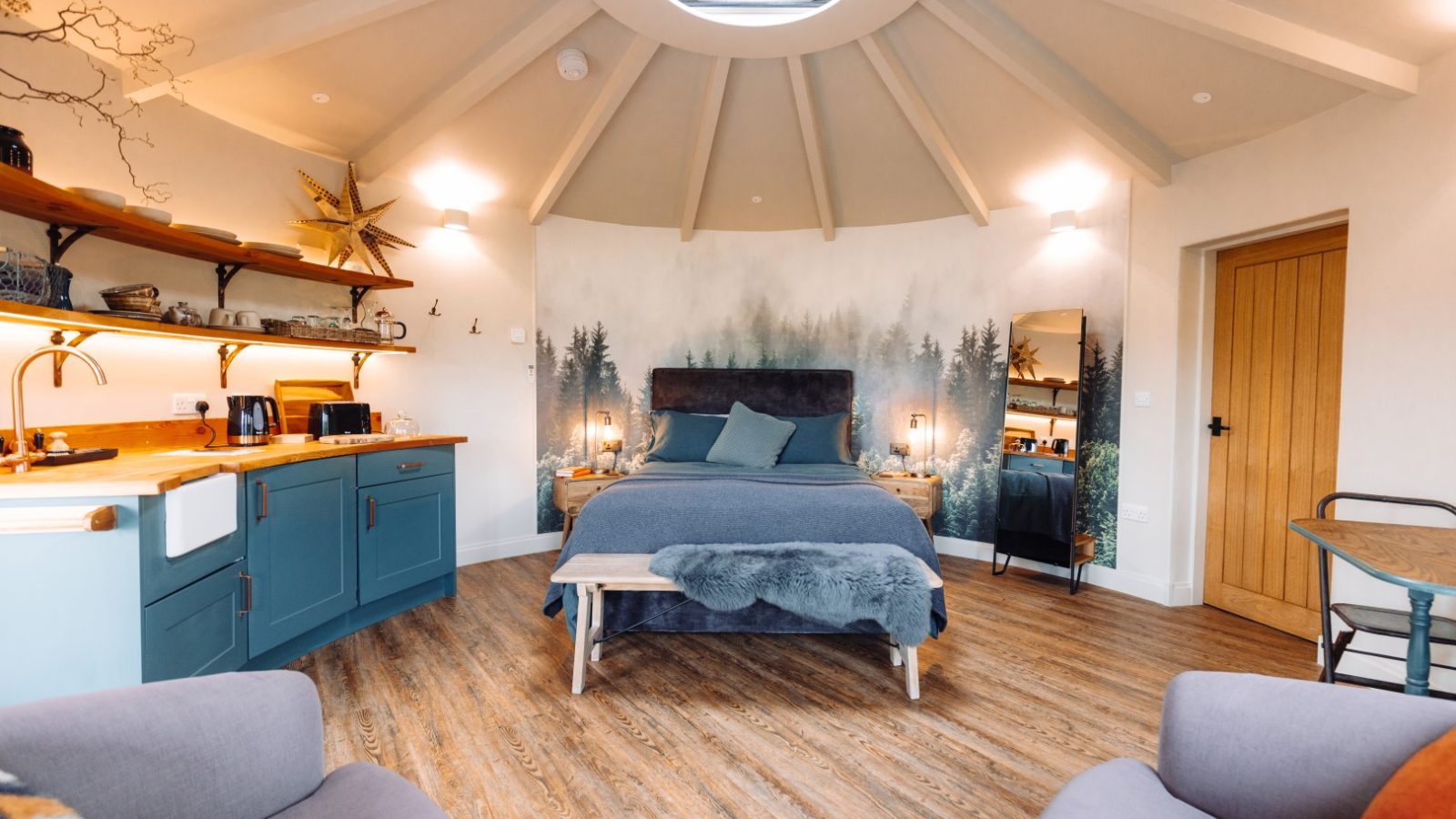 Experience a unique retreat in this circular room featuring wood flooring and a bed against a forest-themed mural. Relax in the cosy seating area under the skylight, enjoy the small kitchen, and make the most of convenient laundry services for a truly refreshing stay.