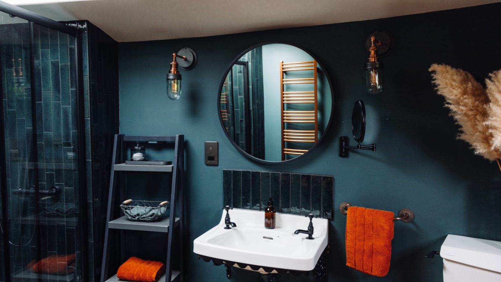 Modern bathroom retreat with dark green walls, round mirror, black fixtures, and orange accents.