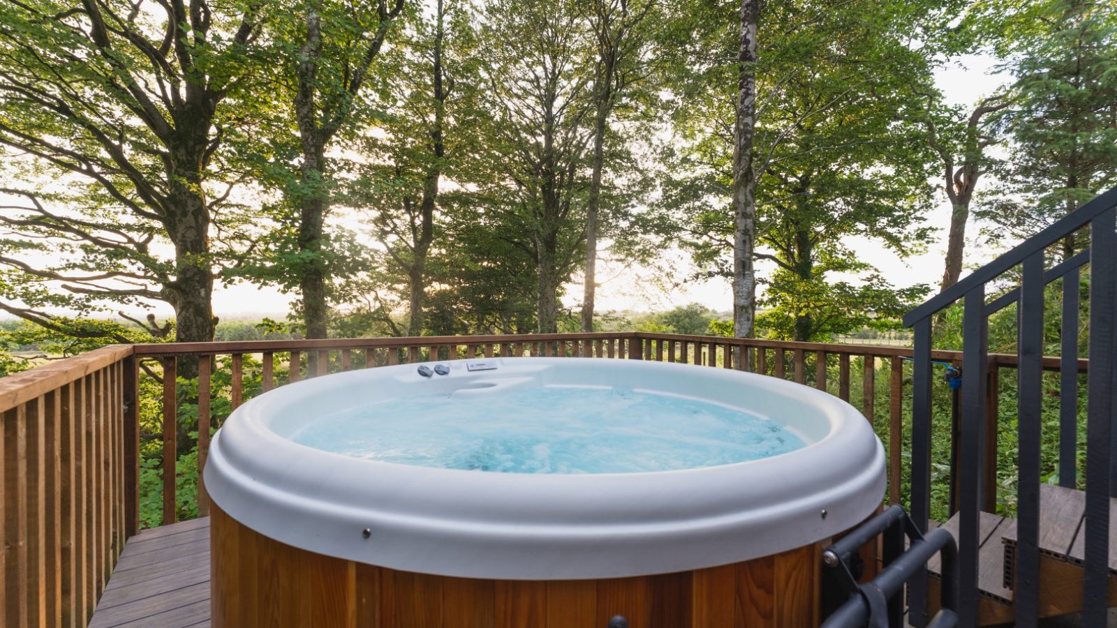 Nestled within Cuckoos Hideaway, a wooden hot tub sits invitingly on a deck surrounded by trees. Bubbling water beckons as you ascend the stairs to this serene oasis, where nature's embrace envelops you in tranquility and relaxation.