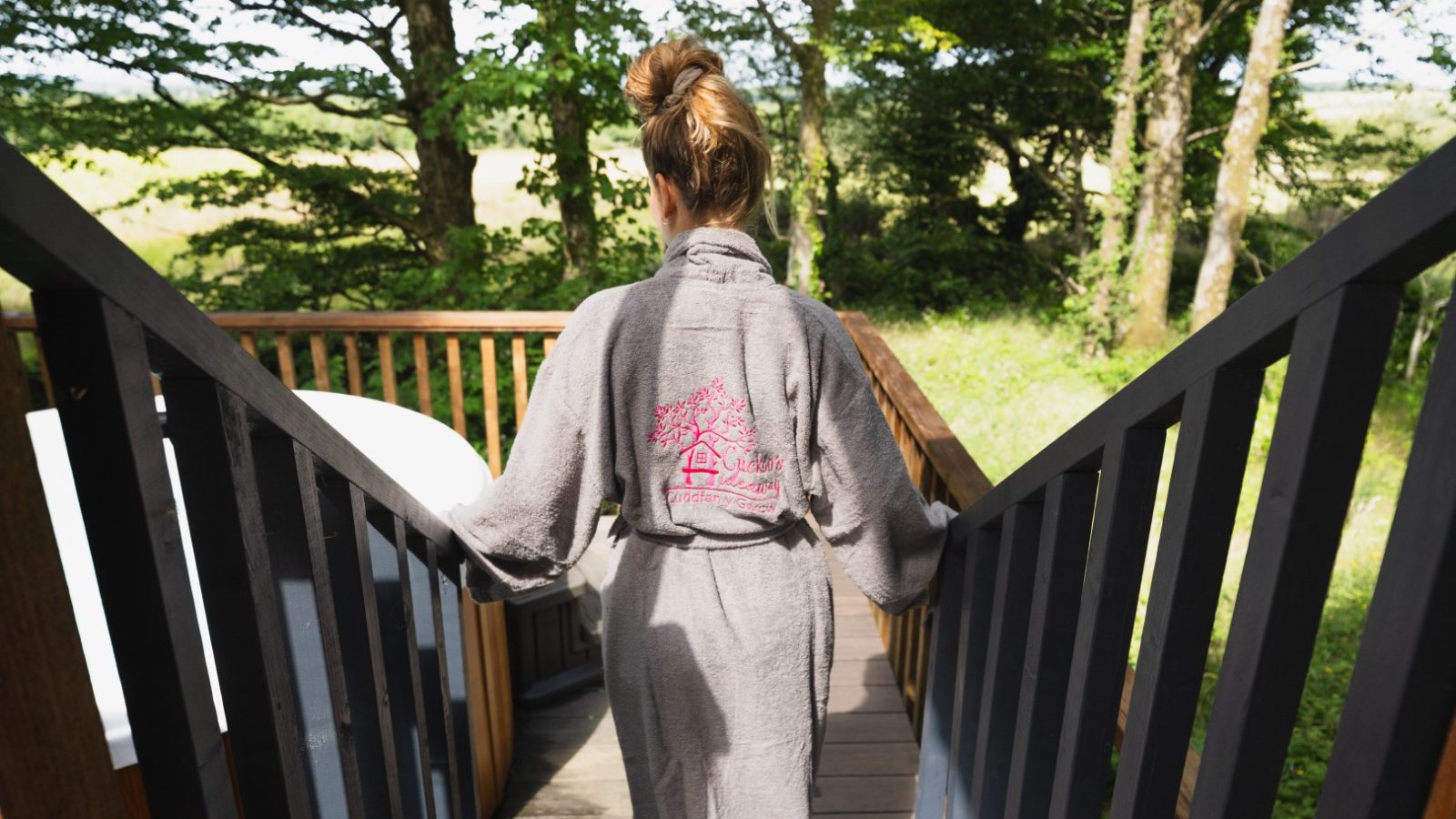 A person in a gray robe descends the wooden stairs, embraced by the serene whispers of the forest. This enchanting trail leads deeper into Cuckoos Hideaway, where nature’s secrets linger in every shadow and rustling leaf.