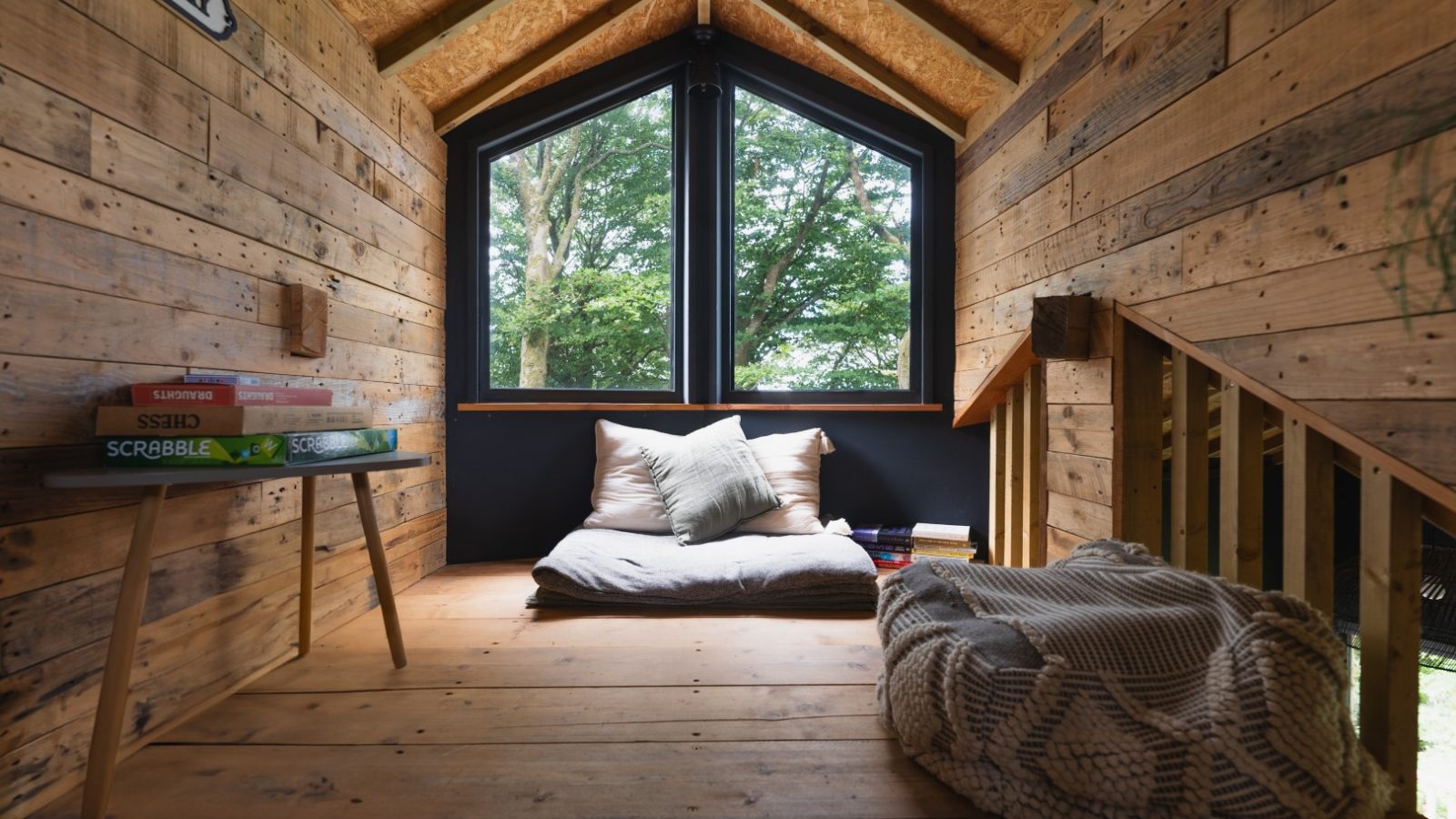 Cuckoos Hideaway offers a cozy loft with wooden walls, a large window, floor cushions, books, and a comfy pouf.