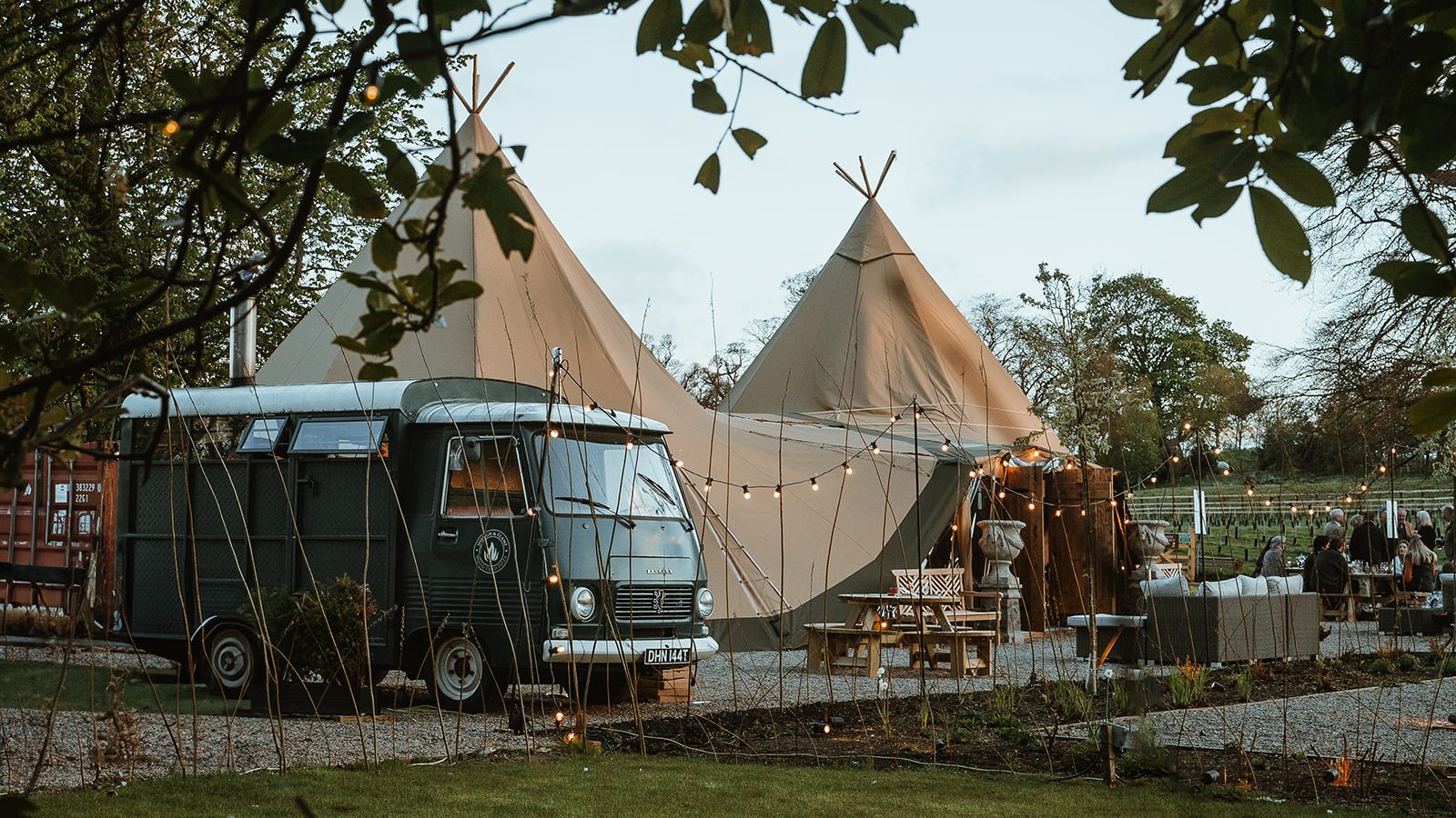 Celebrate your September wedding with an enchanting outdoor reception. Nestled in a serene garden, enjoy a UK staycation ambiance featuring a vintage van, tipi tents adorned with string lights, and charmingly arranged tables for an unforgettable evening under the stars.