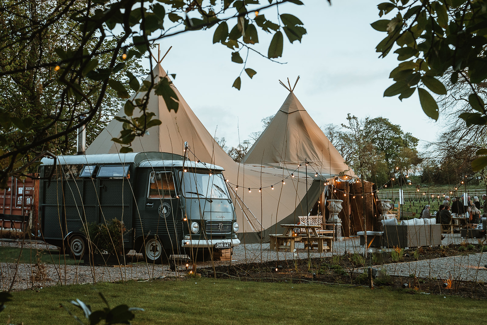 Celebrate your September wedding with an enchanting outdoor reception. Nestled in a serene garden, enjoy a UK staycation ambiance featuring a vintage van, tipi tents adorned with string lights, and charmingly arranged tables for an unforgettable evening under the stars.