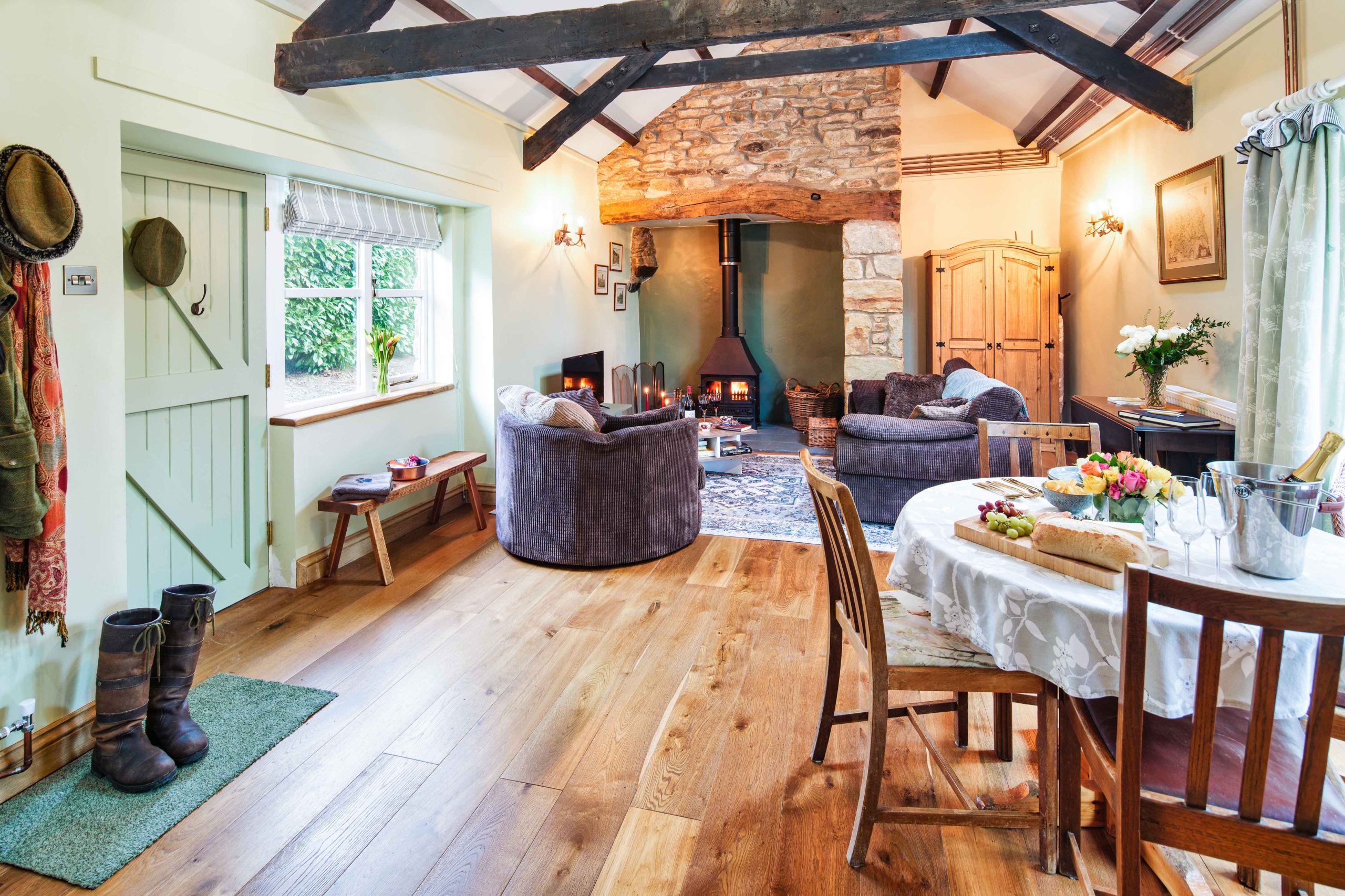 Cozy rustic living room perfect for a September UK staycation, featuring exposed beams, a stone fireplace, round chairs, and a wooden dining table adorned with decorative items.