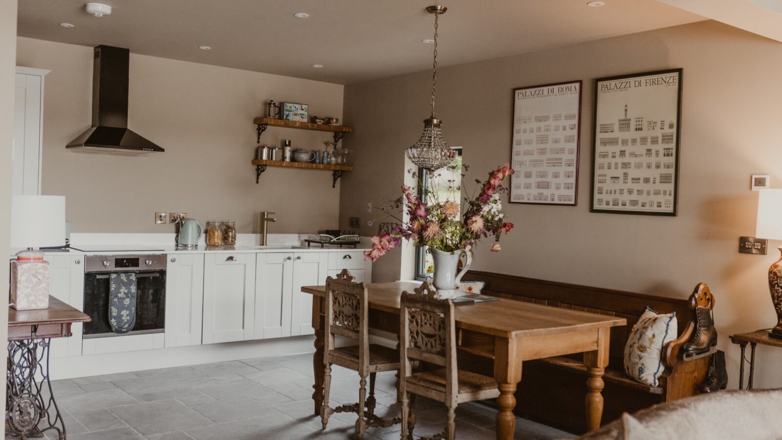 Cozy kitchen with white cabinets, wooden dining table reminiscent of a charming Boat House, hanging light fixture, and decorative items on shelves and table.