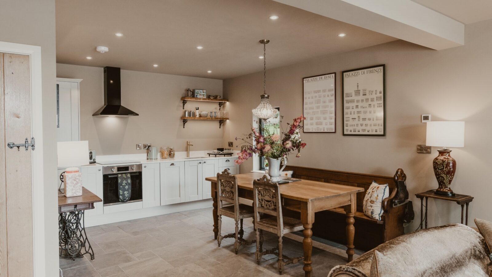 The Boat House features an open-plan kitchen and dining area with a wooden table, white cabinets, wall art, and soft lighting.