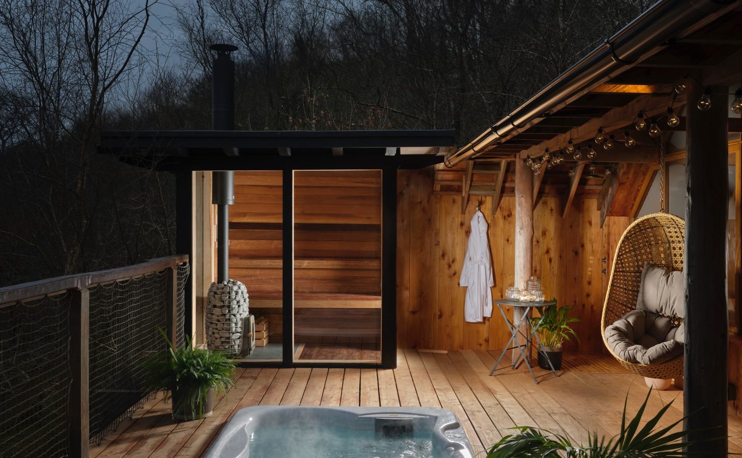 Outdoor deck featuring a hot tub, hanging chair, and a wooden sauna at dusk, nestled in the serene Wolf Wood Treehouses.