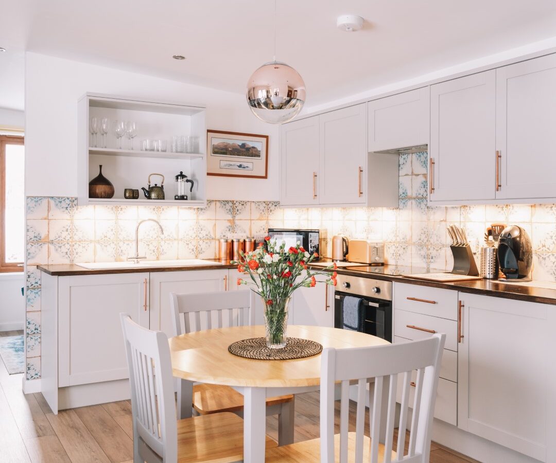 Modern kitchen with white cabinets, tiled backsplash, wood floor, round table with chairs, and hanging light fixture—perfect for Frances to spread out her art supplies on a lazy afternoon.