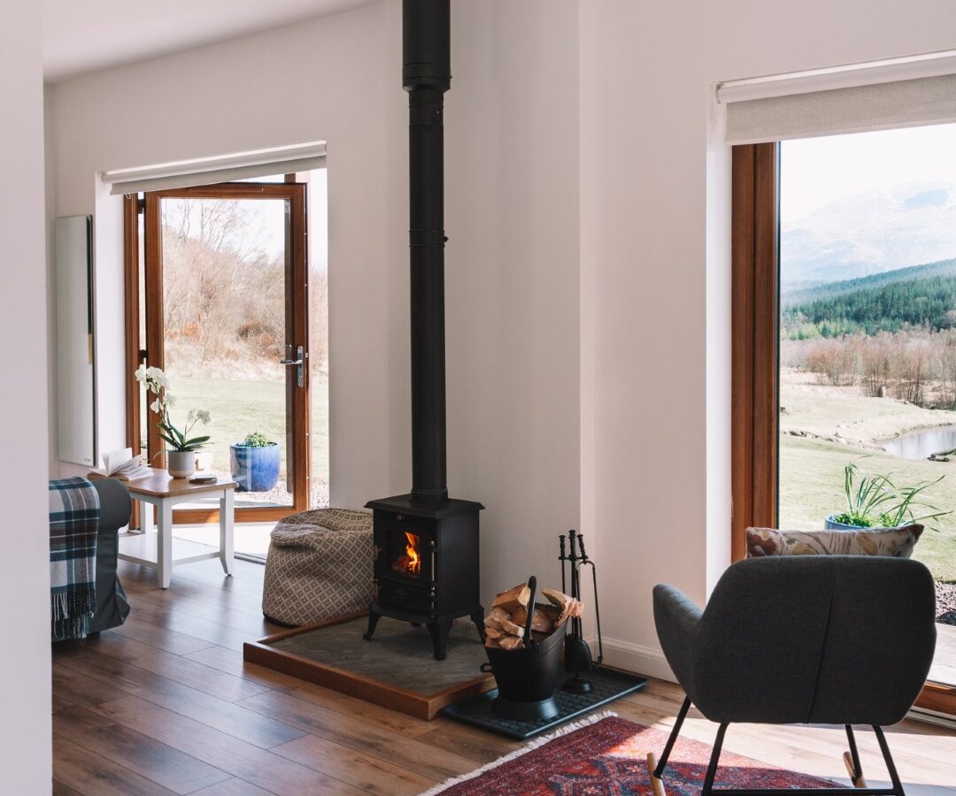 Cozy living room with a wood-burning stove, large windows offering a scenic view, and a rug. A perfect nook is set up for artists, featuring Frances Sketch Pad and drawing tools among the comfortable seating. It's an inviting space where creativity meets comfort.