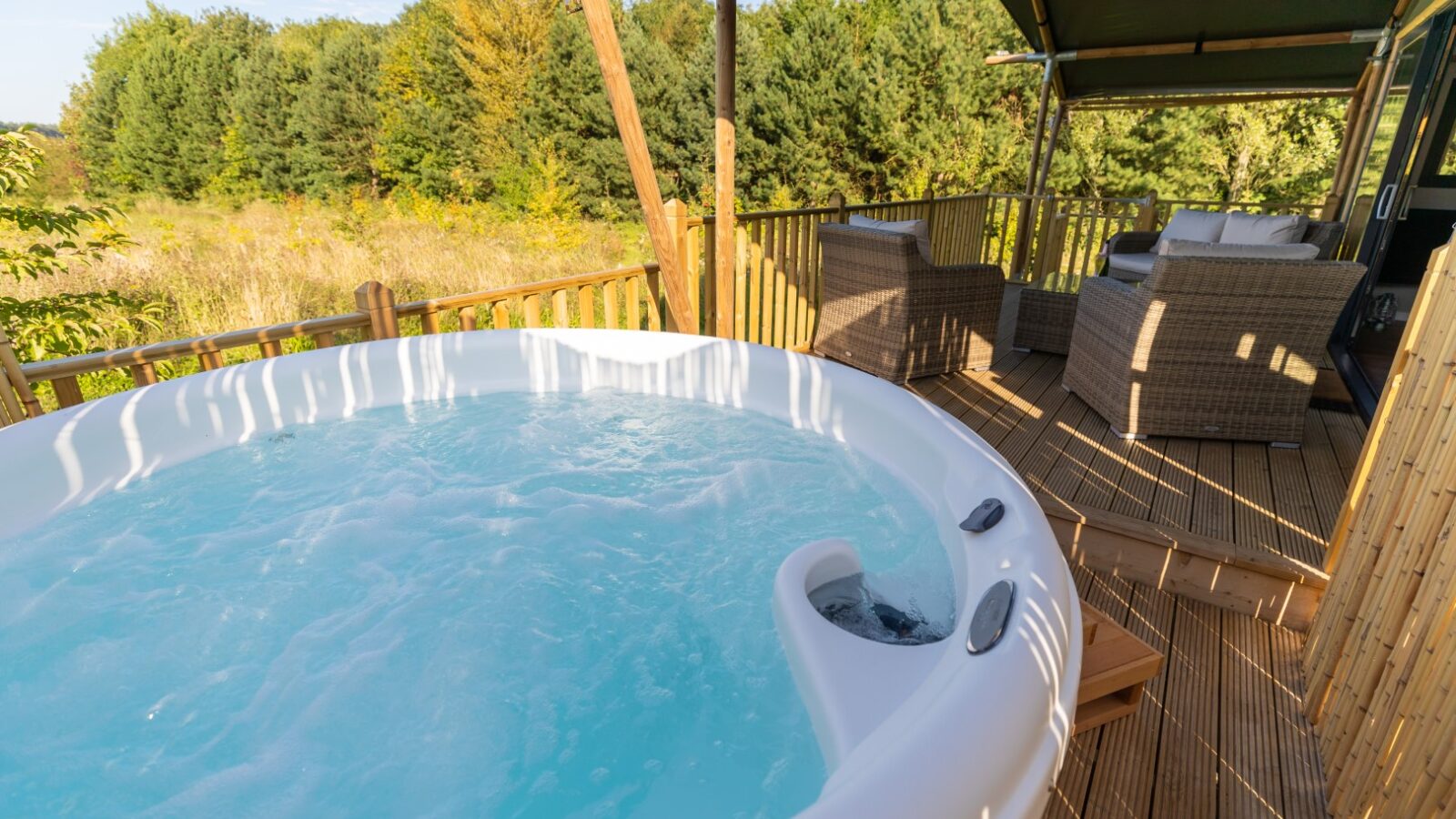 Nestled in the serene landscape of Birdholme, this outdoor hot tub on a wooden deck offers a perfect glamping experience. Surrounded by lush greenery and trees, relax beside the elegant wicker furniture and enjoy nature's tranquility.