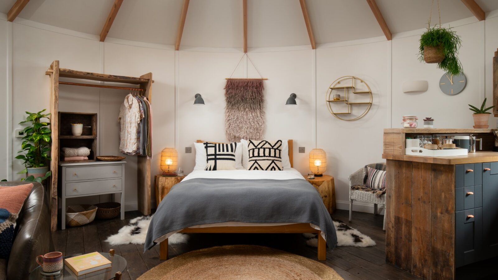 Cozy room with a nest-like bed, wooden decor, open wardrobe, wall plants, and circular rug, featuring soft lighting and earth tones.