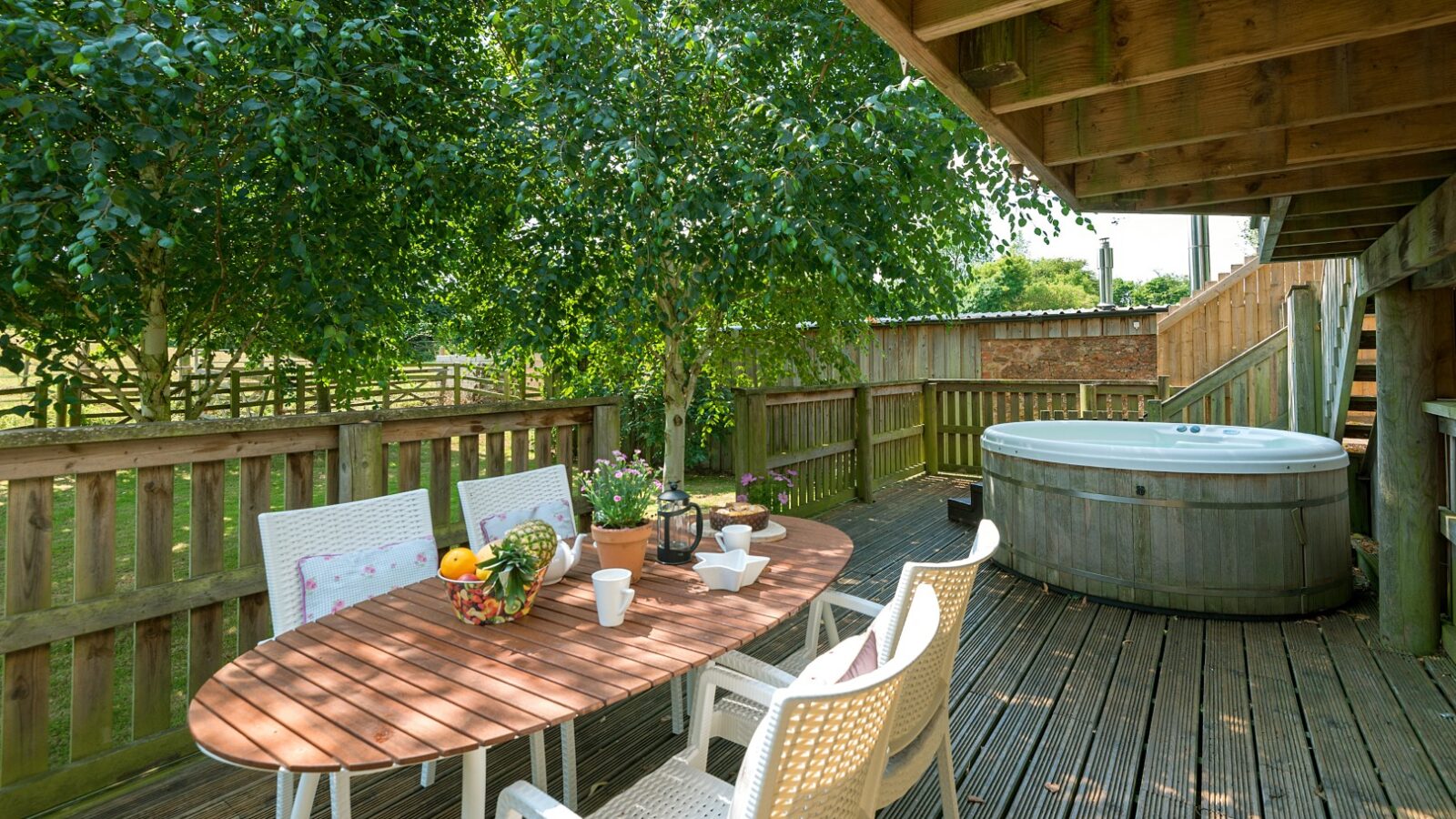 Nestled at Lavender Hill, this outdoor wooden deck offers a charming dining table set for four, a rejuvenating hot tub, and lush surrounding greenery. Perfect for those seeking unique treehouse accommodation amidst nature's tranquility.