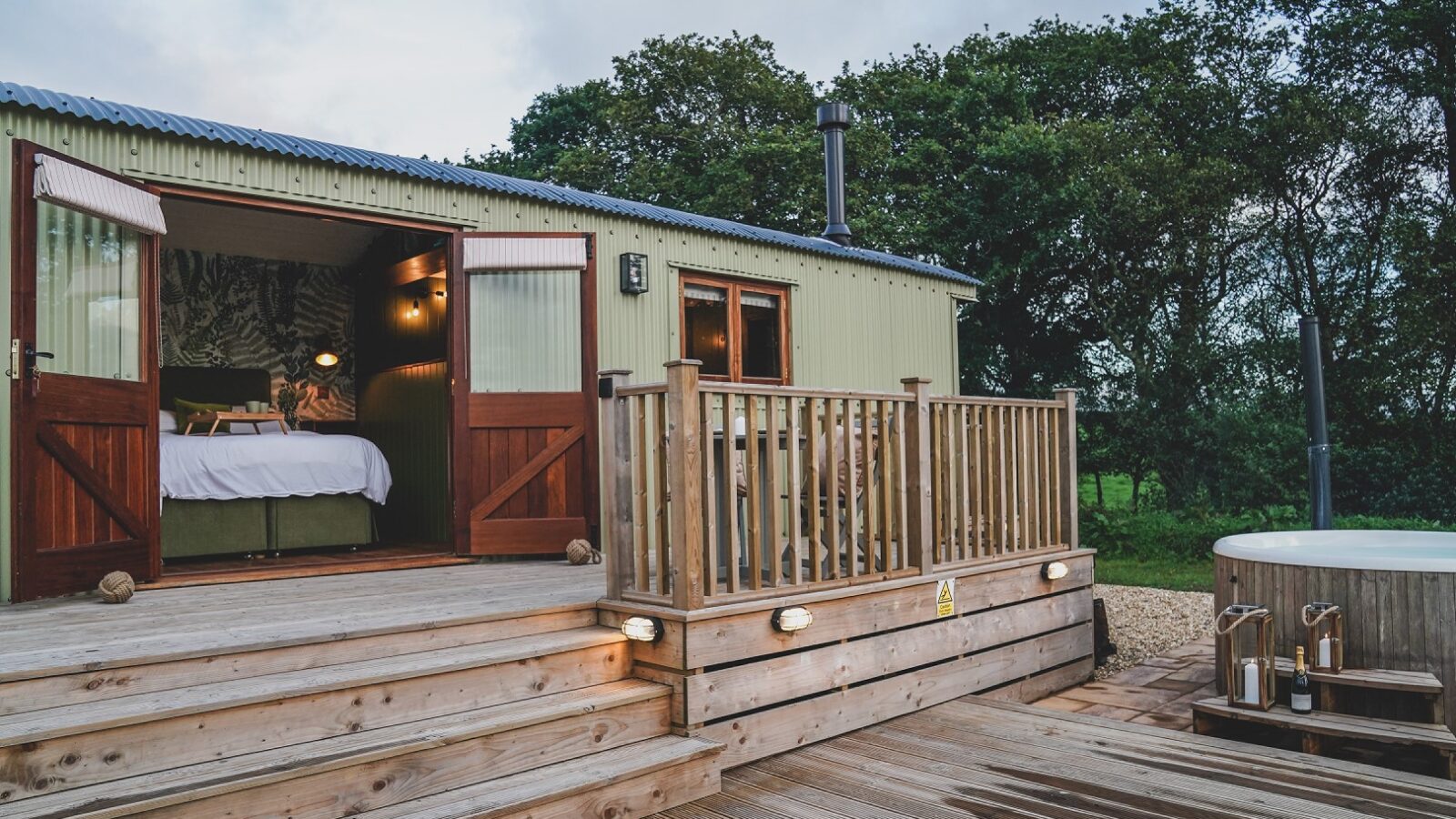 A cozy hideaway, this cabin features open doors, a wooden deck, a hot tub, and a forest backdrop.