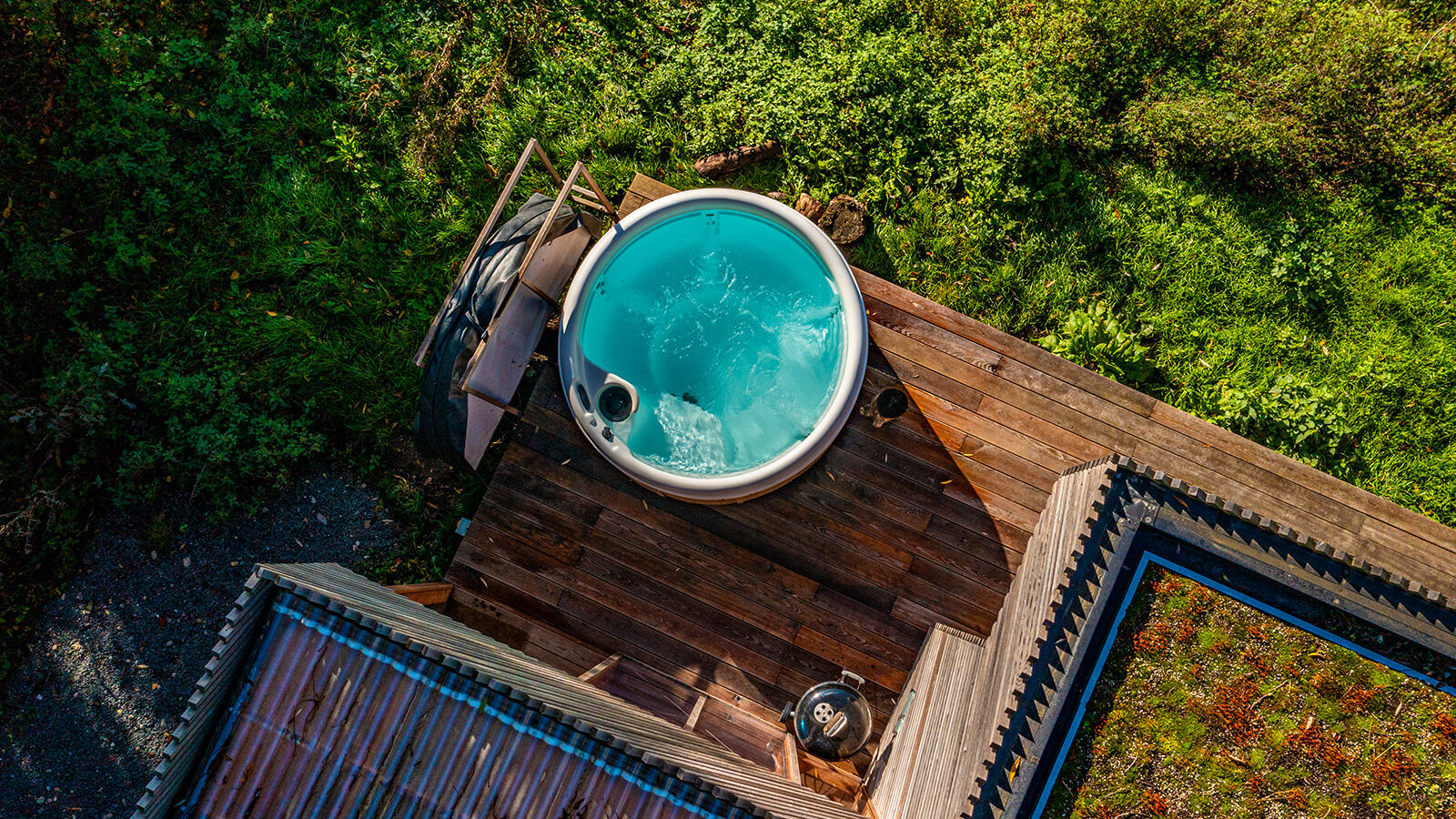 Aerial view of a circular hot tub with bubbling water on a wooden deck, nestled amidst lush green foliage. It's the perfect hidden gem for tranquil escapes, reminiscent of the serene retreats offered by Browning Bros and Secret Escapes.