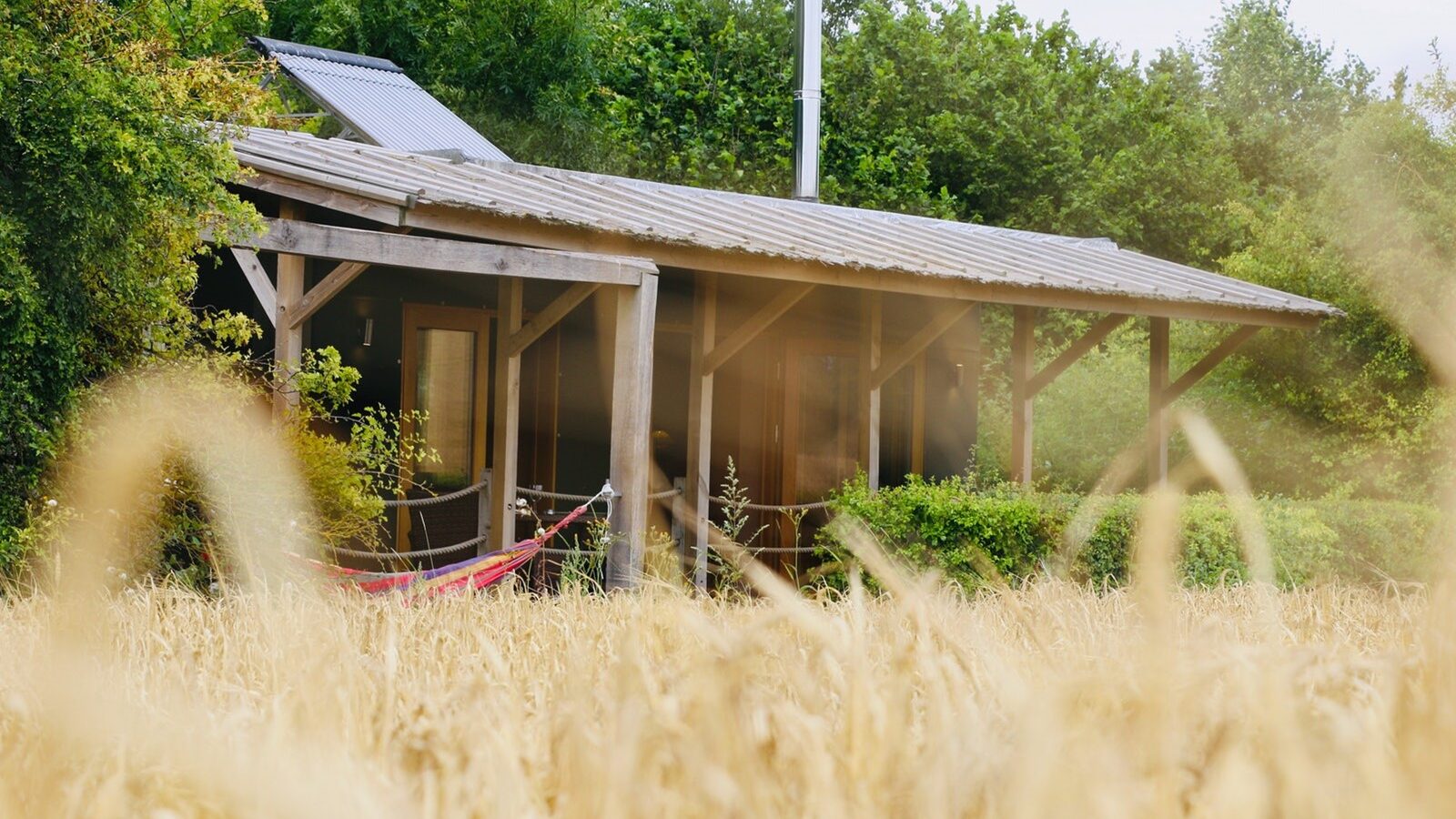 Nestled in the heart of the Chilterns, this rustic wooden cabin boasts a metal roof and a cozy red hammock on the porch. Surrounded by lush greenery and an open field, it's the perfect escape at Chilterns View Lodges.