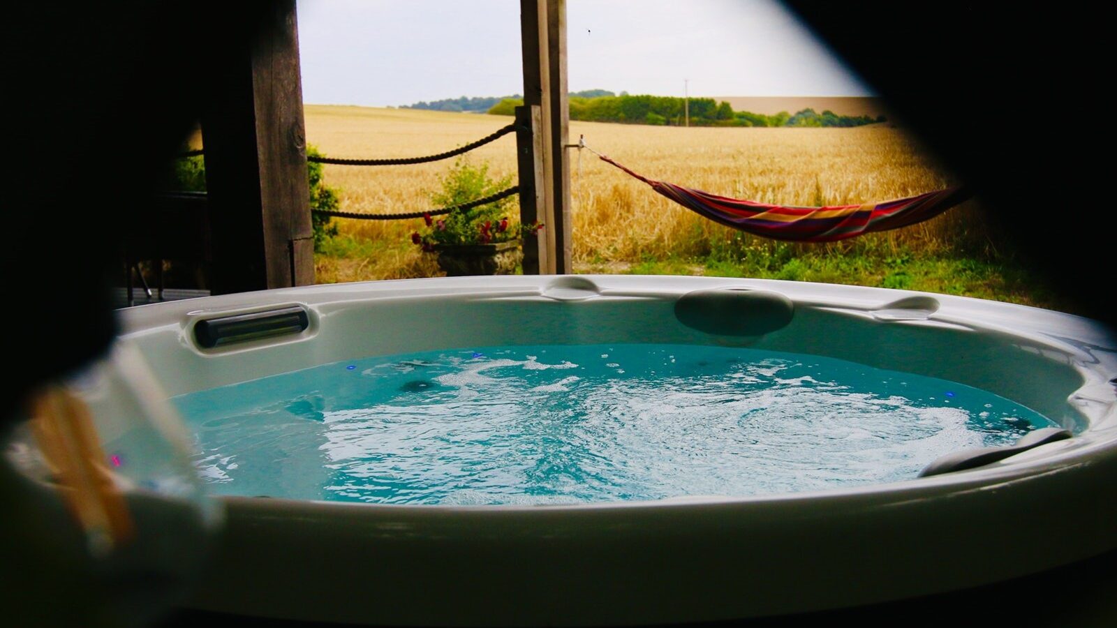 A hot tub on the patio of the View Lodges overlooks a field with a hammock hanging nearby, offering a serene escape in the heart of the Chilterns.