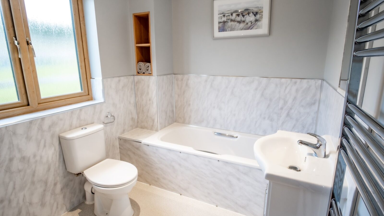 A modern bathroom in Lundy Lodges features a white bathtub, toilet, and sink. Marble-style walls and a towel rack add to the elegance.