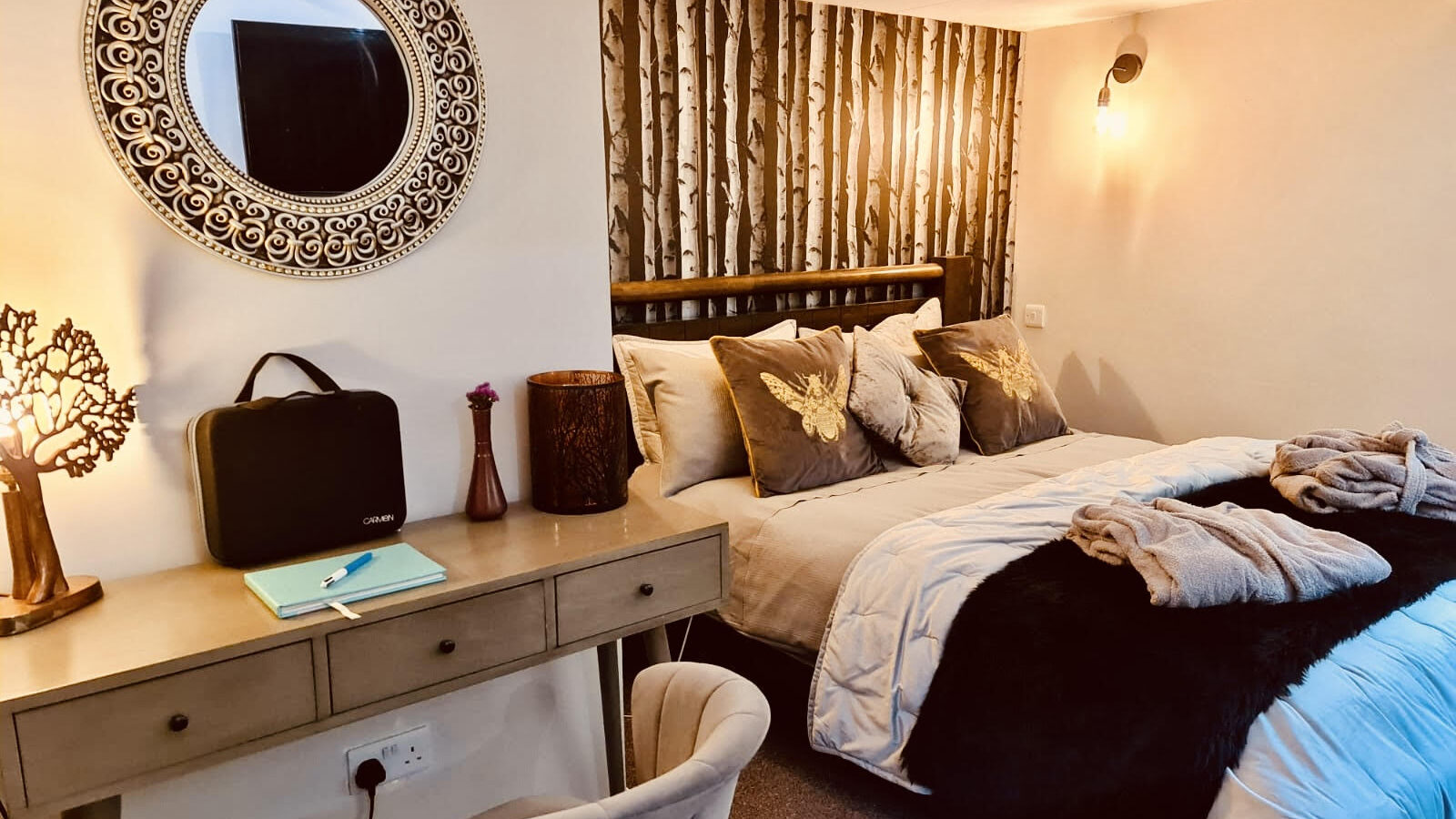 Cozy bedroom with a double bed, forest-themed decor, and a round mirror in this star-gazing treehouse. A desk with a chair and soft lighting complete the ambiance.