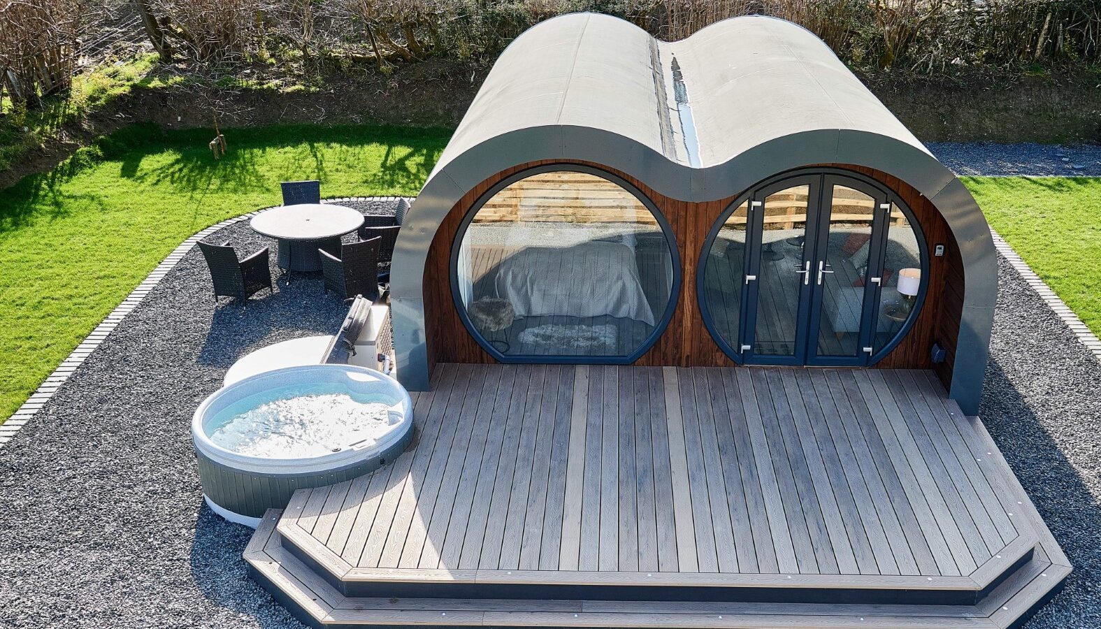 Nestled in the scenic Camlad Valley, this modern pod cabin boasts circular windows, a wooden deck, and an outdoor hot tub. Experience tranquility surrounded by a gravel yard and lush greenery in one of the finest Luxury Pods available.