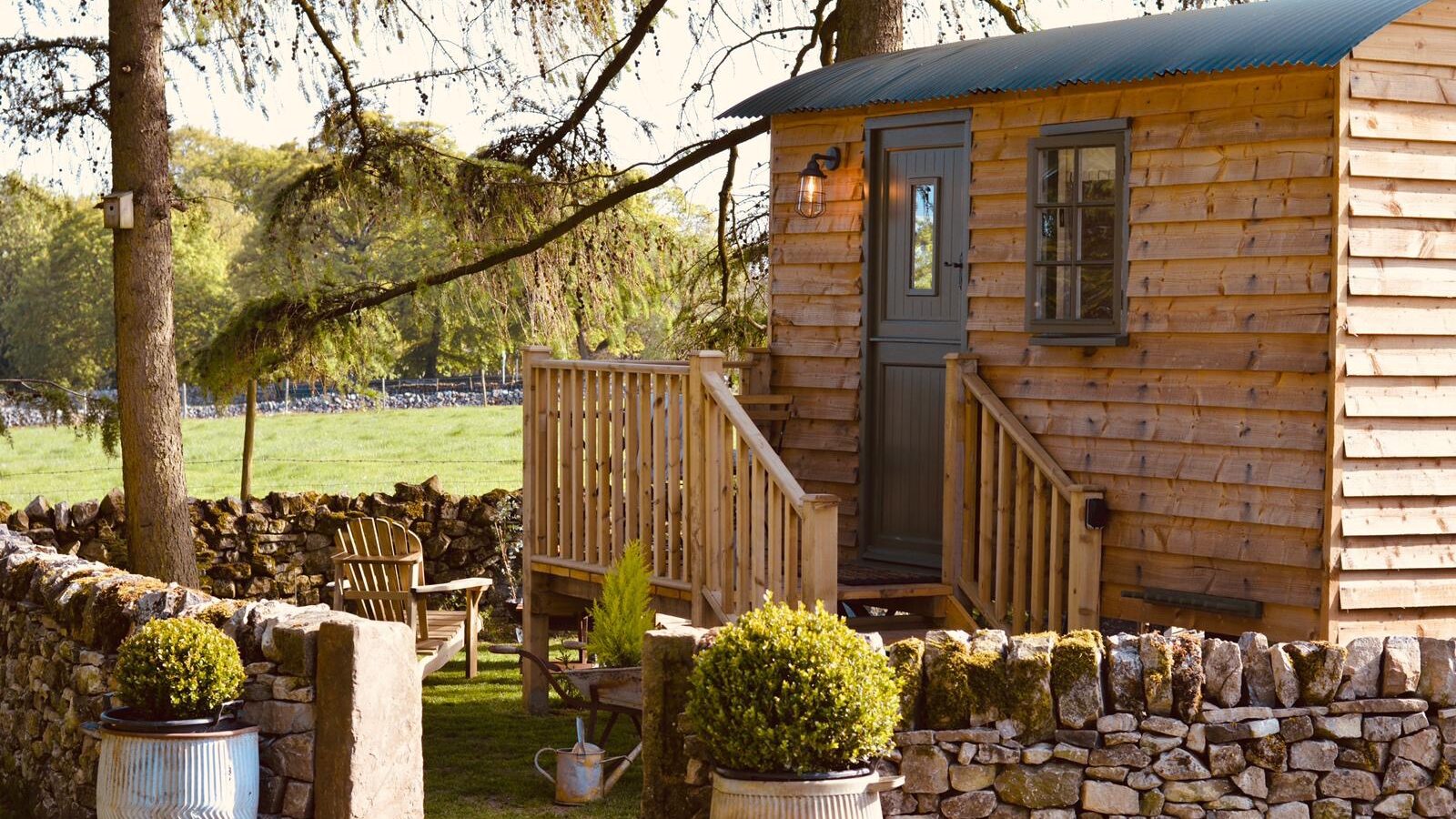 Nestled amidst stone walls and trees, this charming wooden cabin with a small porch offers tranquility. Evoking the rustic charm of Shepherds Huts, the garden area features inviting chairs and planters. A serene escape in Smithyfields awaits.