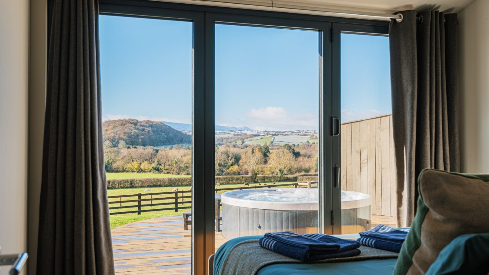 Bedroom with large glass doors at Pontypinna Hideaways, offering a patio hot tub and scenic countryside views.