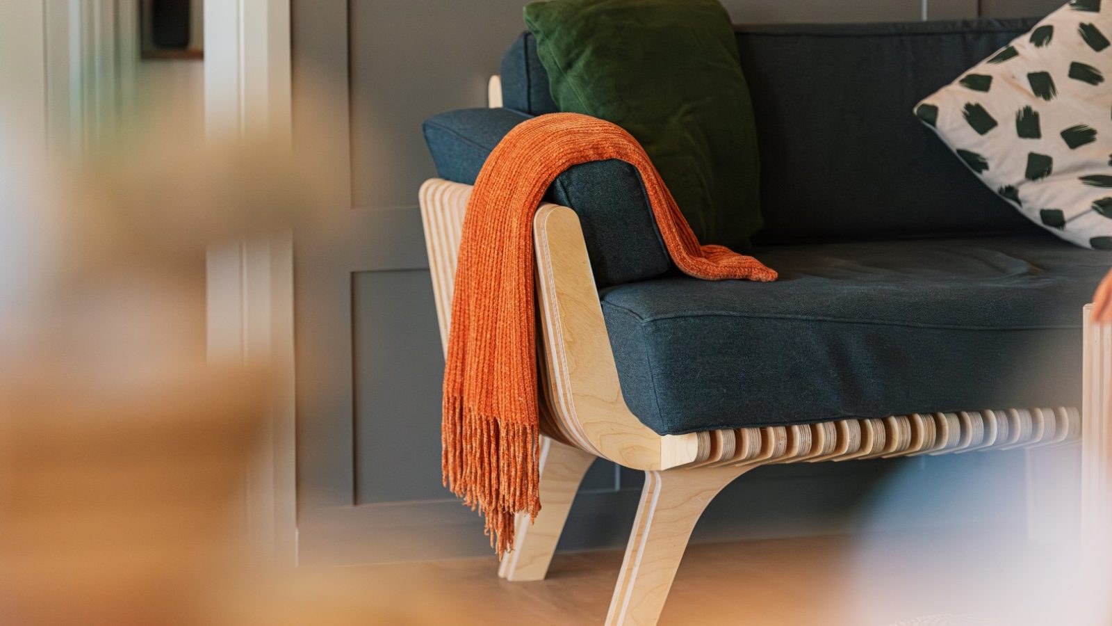 Modern Pontypinna Hideaways sofa with a dark cushion, green pillow, and orange blanket against a paneled wall.