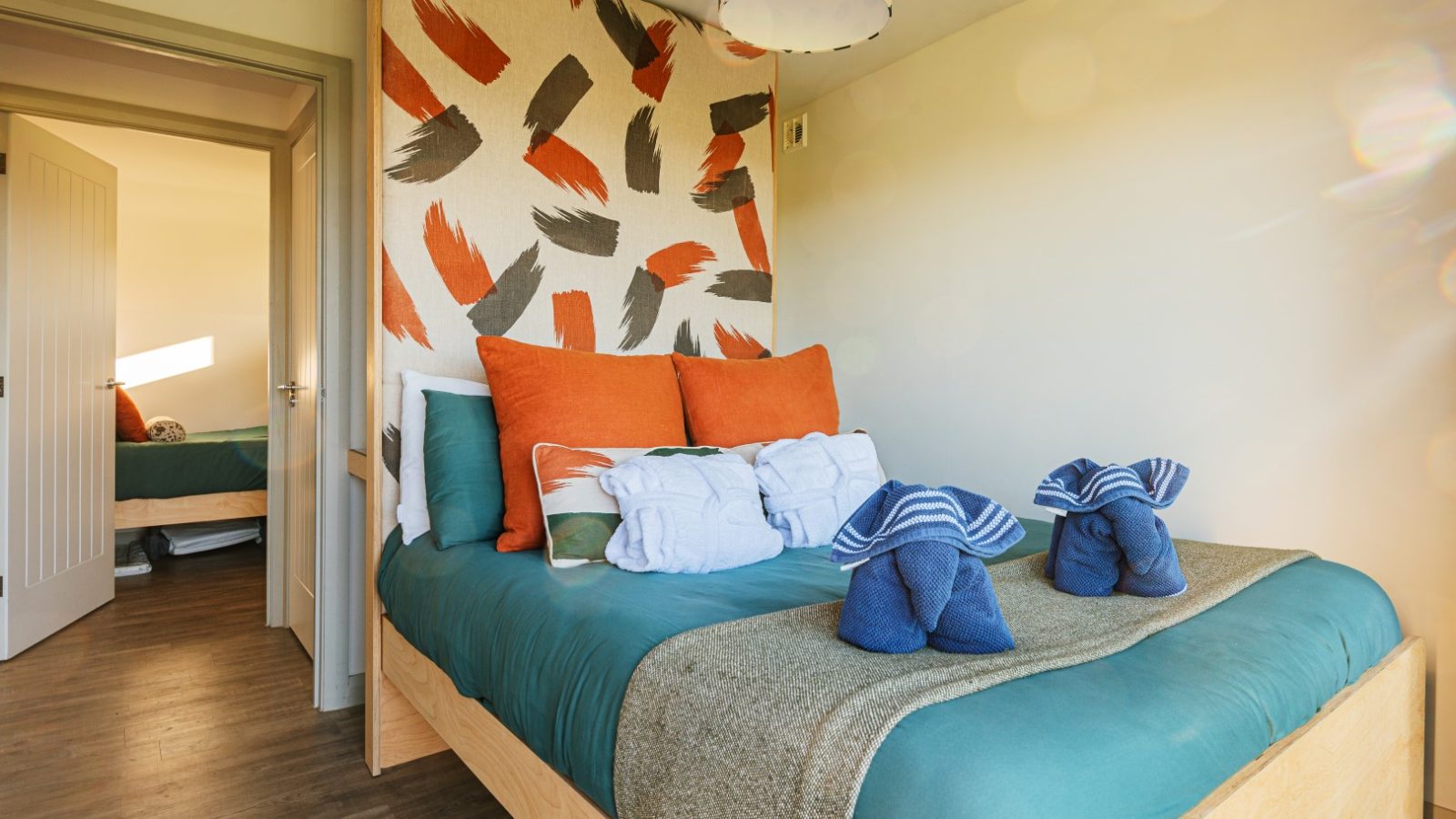 Pontypinna Hideaways: A modern bedroom showcases colorful pillows and towel sculptures, with an open door leading to another room.