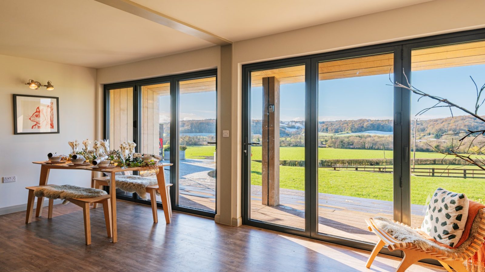 Modern dining area with large windows, wooden flooring, and outdoor view of lush Pontypinna Hideaways' fields and hills.