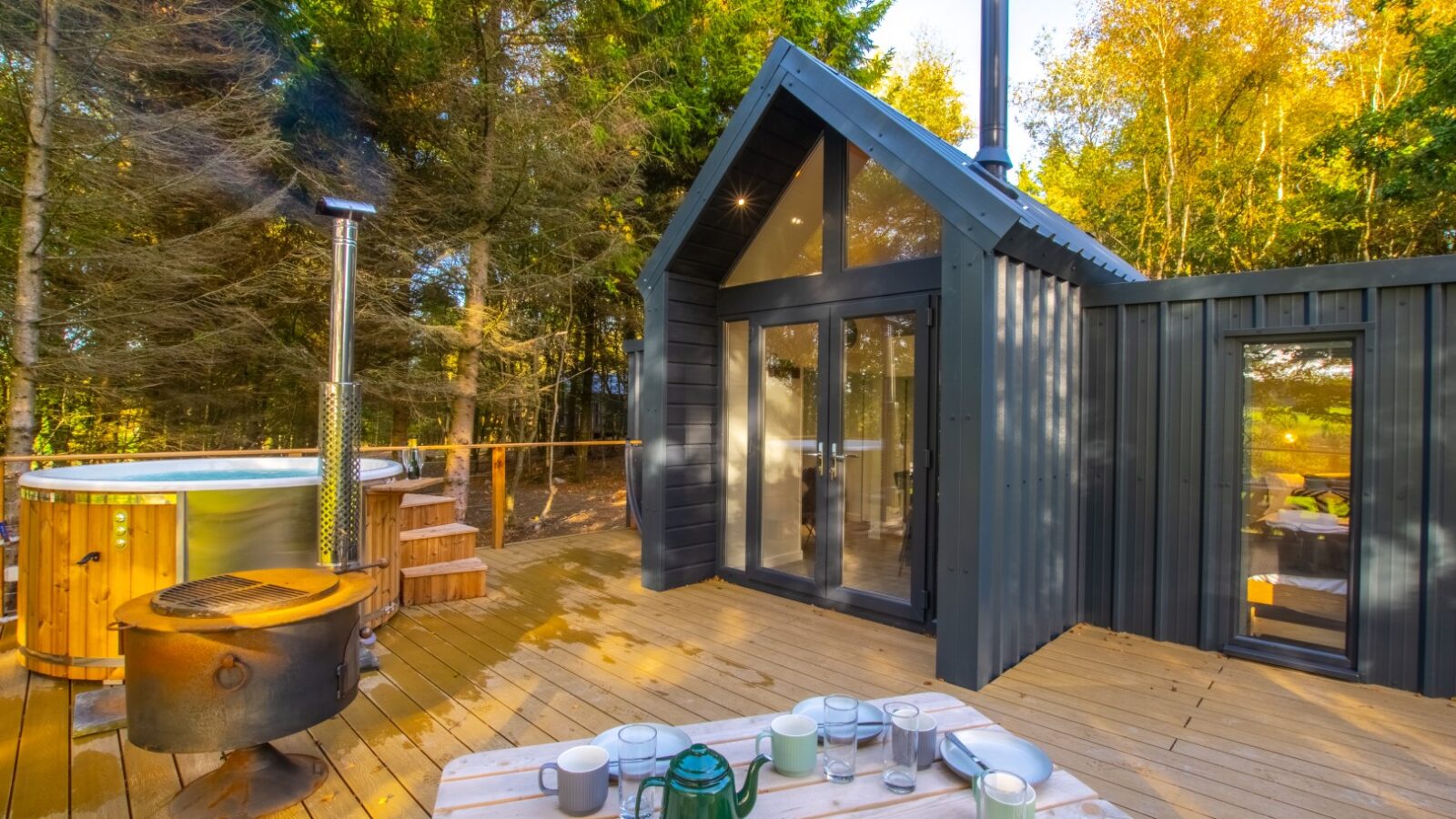 Escape to a cozy cabin in the woods for the ultimate glamping experience. Enjoy glass doors opening to breathtaking views, a hot tub for relaxation, and a picnic table set for breakfast on a wooden deck surrounded by towering trees. Perfectly nestled near Porth Eryri.