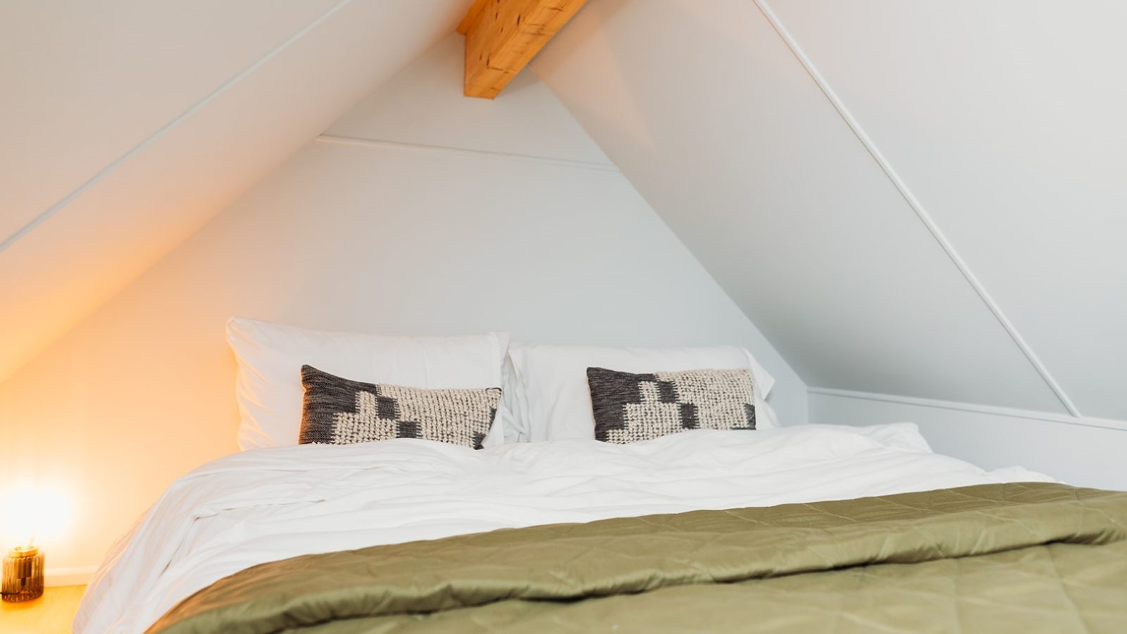 Nestled in a cozy attic, this Porth Eryri bedroom features a double bed accented with white pillows and patterned cushions. A green quilt adds warmth under the slanted ceiling, creating a perfect retreat.