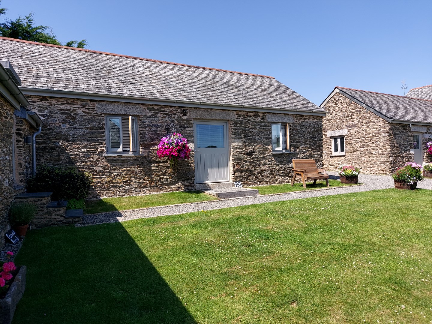 Nestled among blooming flowers, this stone cottage boasts a slate roof and a charming door. A bench and lush lawn make it one of the best places to stay in Cornwall with a dog, offering serenity just a short drive from the Eden Project's holiday cottages.