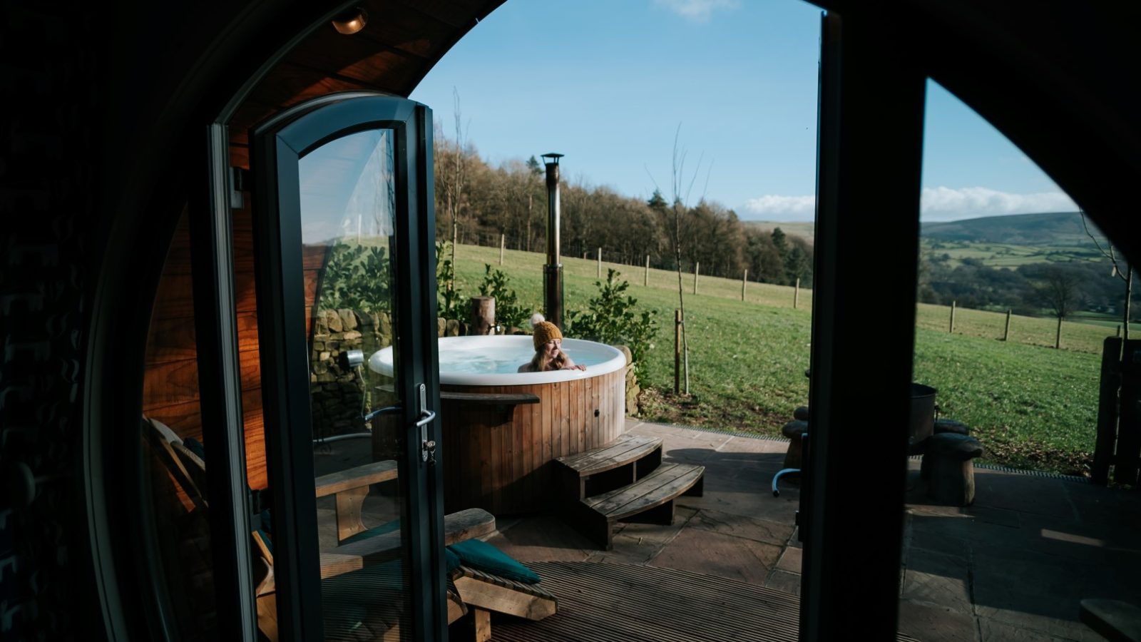 Person relaxing in an outdoor hot tub at Catgill Farm, surrounded by a wooden fence with views of the Yorkshire Dales.