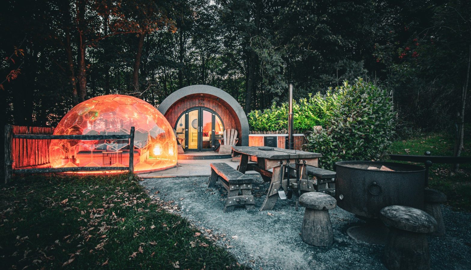 Experience glamping at Catgill Farm in the woods, featuring a lit dome, cabin, outdoor seating, and fire pit.