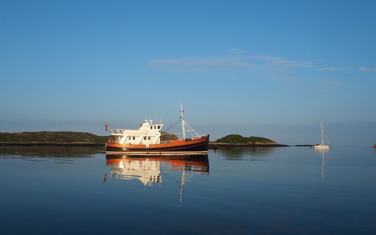 Beneath a clear blue sky, the calm sea cradles a large boat and a small sailboat in the distance, evoking the serene allure of Argyll Cruising.